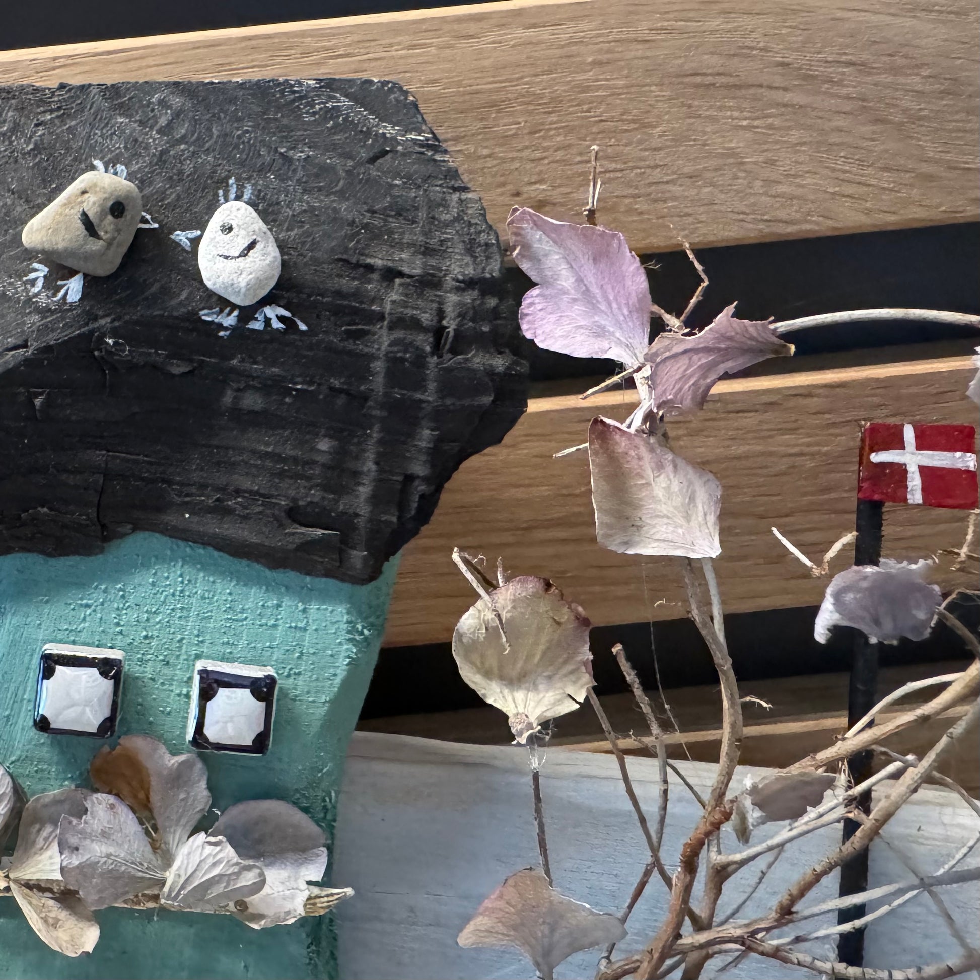 Detailansicht eines maritimen Holzhäuschens mit schwarzem Treibholz-Dach, Fensterdetails und Naturdekoration