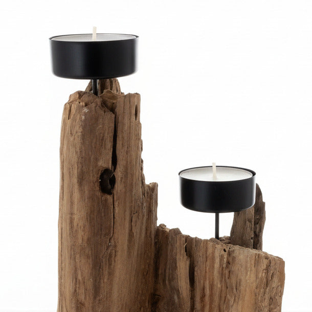 Ein rustikaler Kerzenhalter aus verwittertem Holz. Zwei schwarze Metallkerzenschalen halten weiße Kerzen.