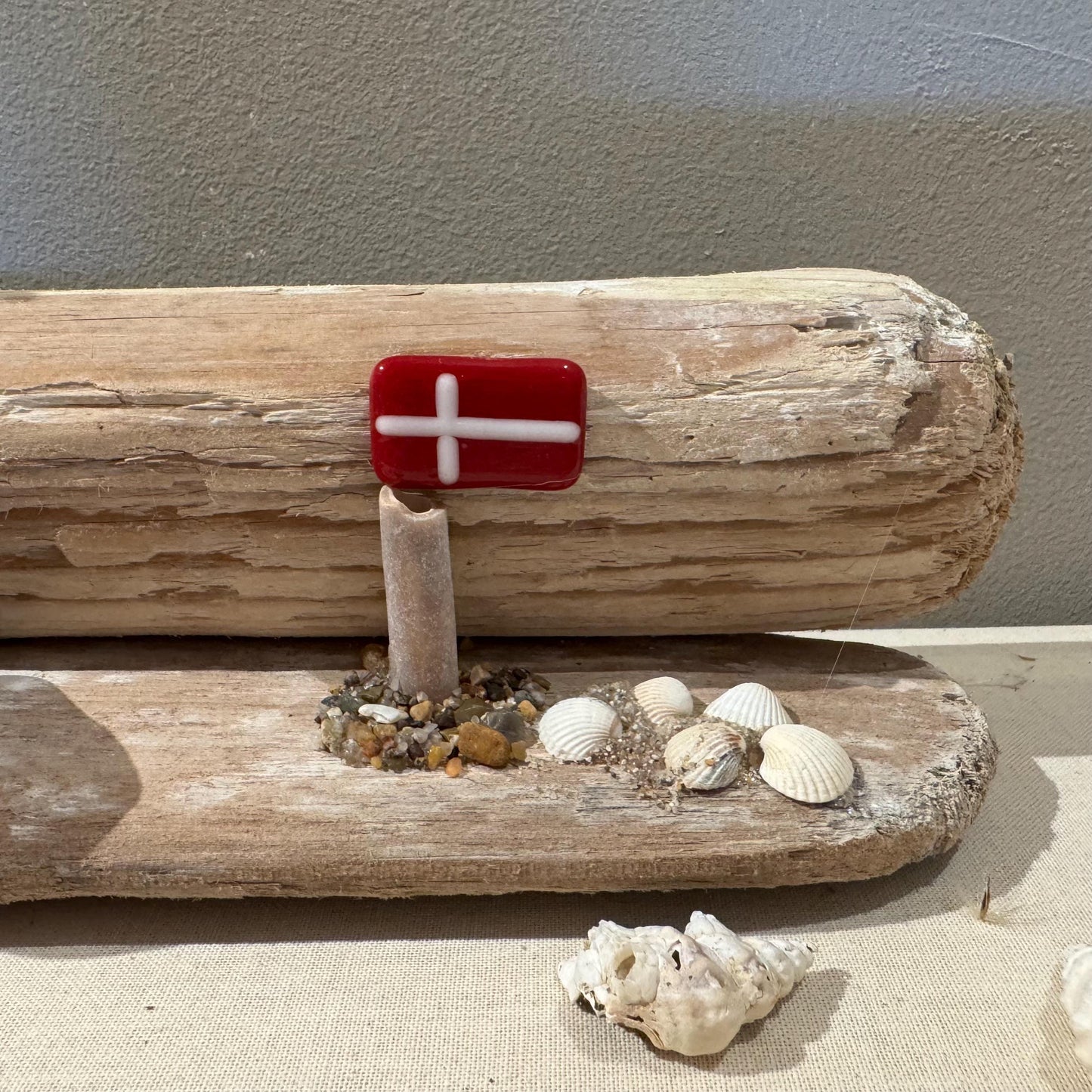 Handgefertigte dänische Flagge aus Glas in einer maritimen Treibholzszenerie mit Naturmaterialien.