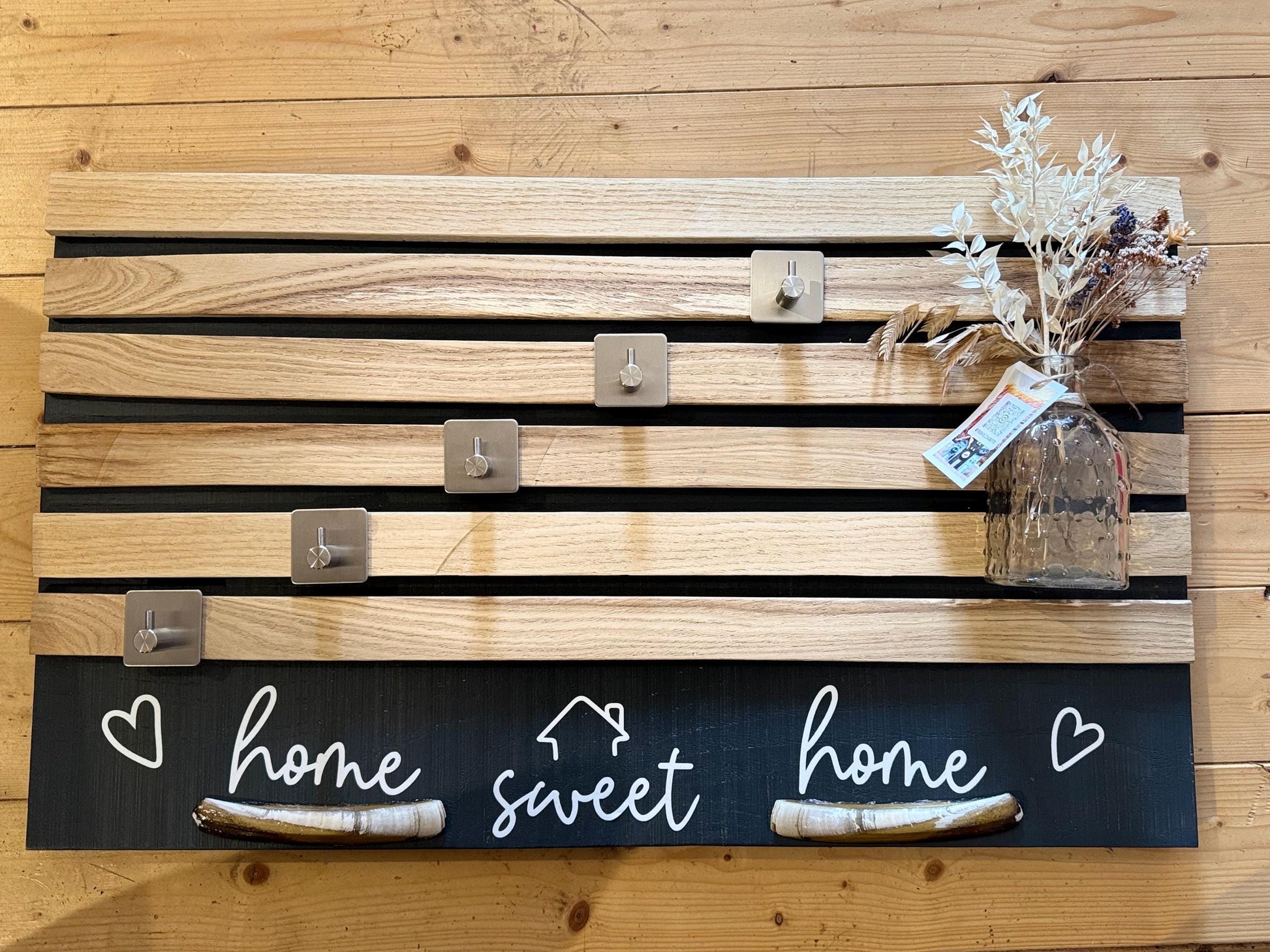 Eine Wandpaneele aus Holz mit horizontalen Holzlatten und Metallhaken. Der untere Teil ist mit den Worten "home sweet home"