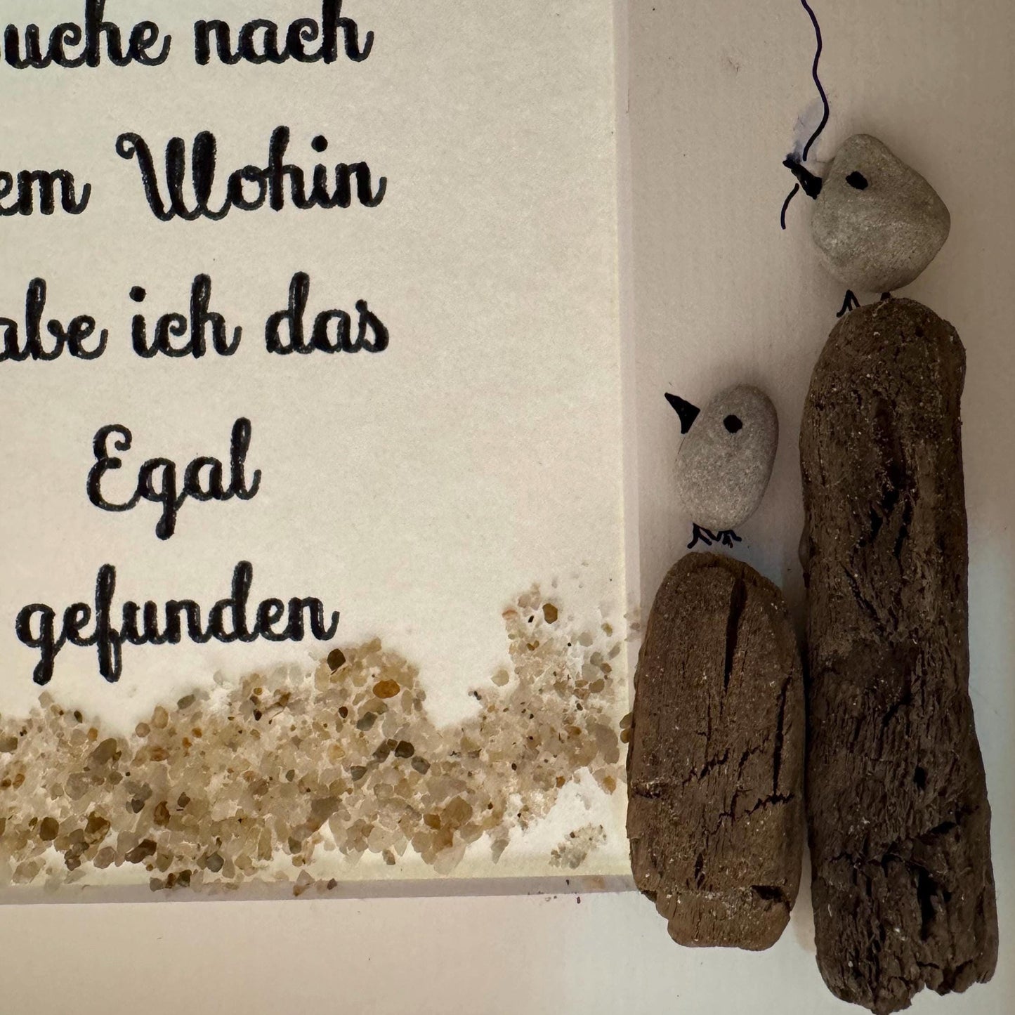 Ein gerahmtes Kunstwerk mit Text und Kieselkunst. Der Text in schwarzer Schrift befindet sich auf weißem Hintergrund