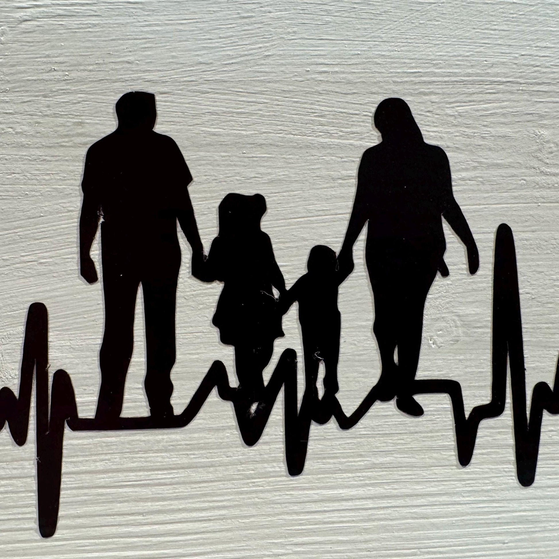 Schwarze Familien-Silhouette, die Hände hält, vor weißem Hintergrund. Die Familie ist durch einen Herzschlag verbunden.