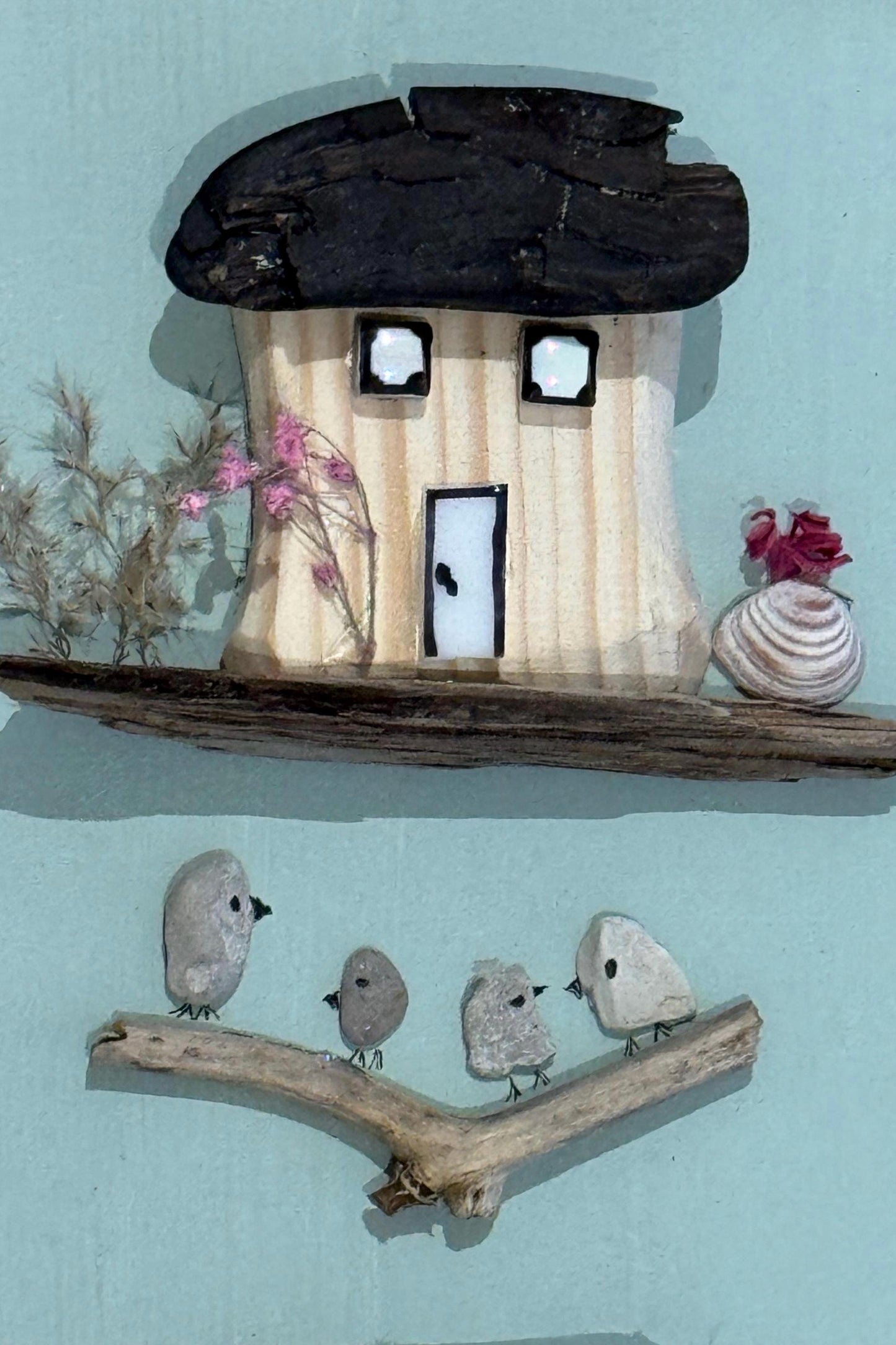 Detailansicht des oberen Hauses mit schwarzem Treibholz Dach, kleinen Fenstern und maritimen Naturdetails.