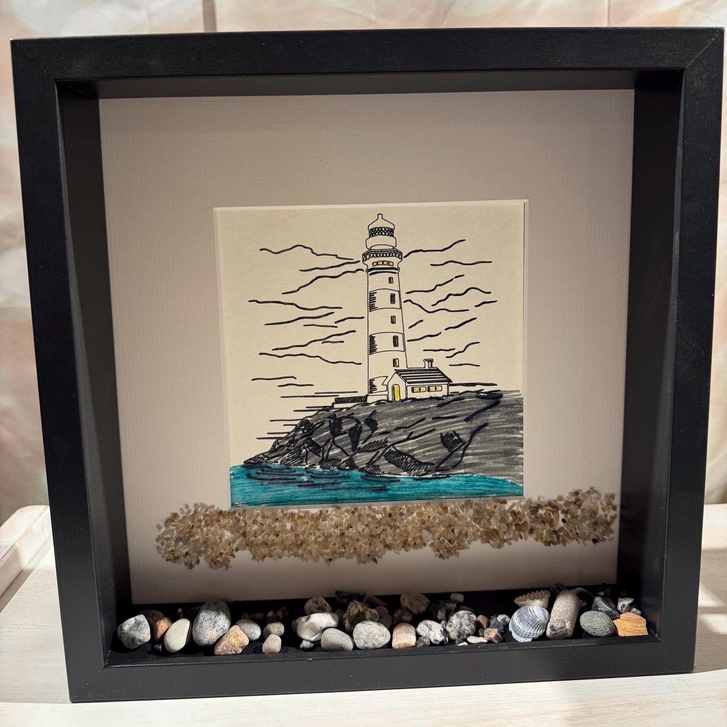 Maritime Wanddeko im schwarzen Holzrahmen: handgezeichnetes Leuchtturm-Bild - nordische Küstenkunst für natürliche Wohnräume.