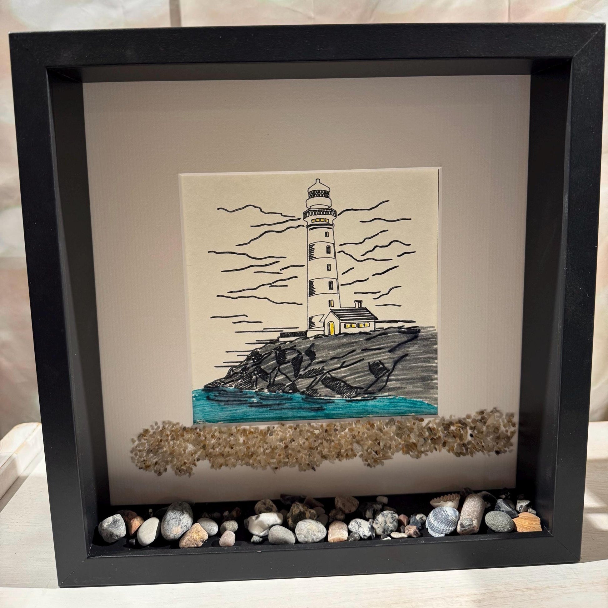 Maritime Wanddeko im schwarzen Holzrahmen: handgezeichnetes Leuchtturm-Bild - nordische Küstenkunst für natürliche Wohnräume.