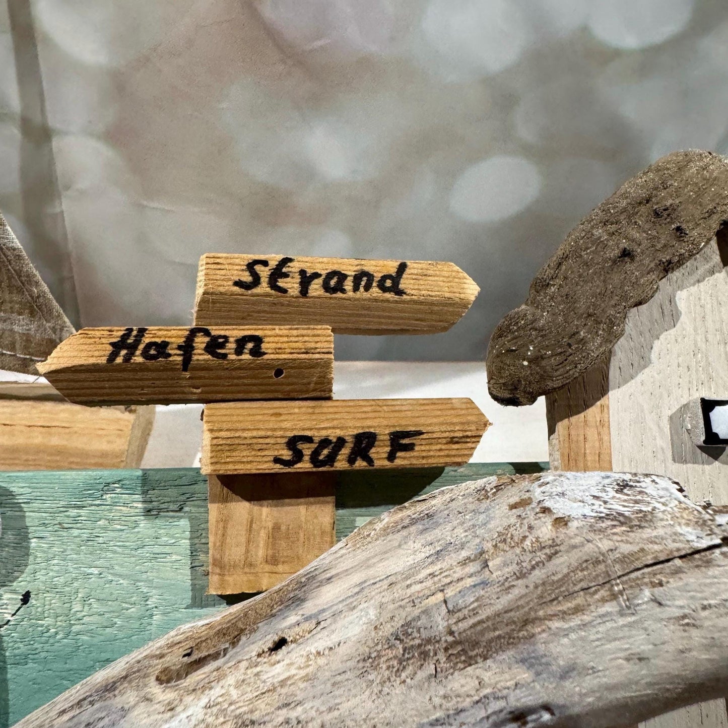 Holzkunstwerk zum Thema Strand mit Richtungsschildern. Die Schilder weisen auf "Strand", "Hafen" und "Surf" hin.