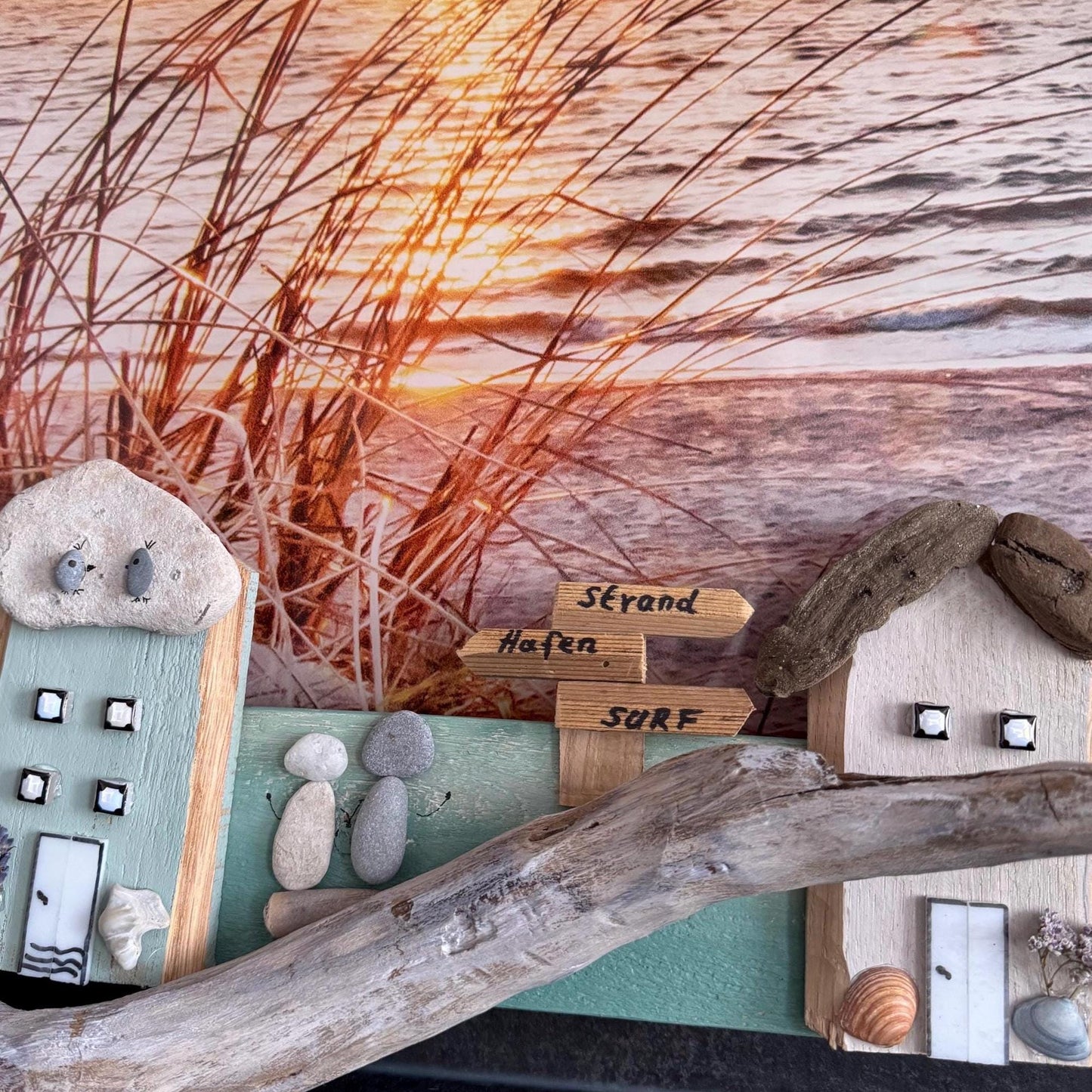 Küstenthemen-Kunstwerk mit Miniaturhäusern und Treibholz. Die Häuser sind aus Holz und Stein gefertigt.