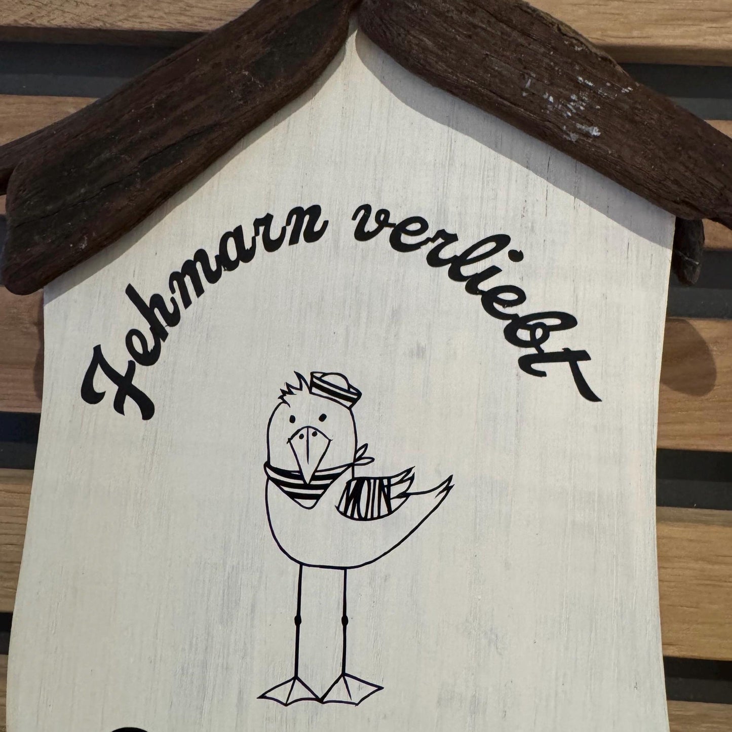 Maritimes Holzhäuschen mit Möwe, Fehmarnsundbrücke und Steinrand - gehalten in einer Hand vor heller Deko.