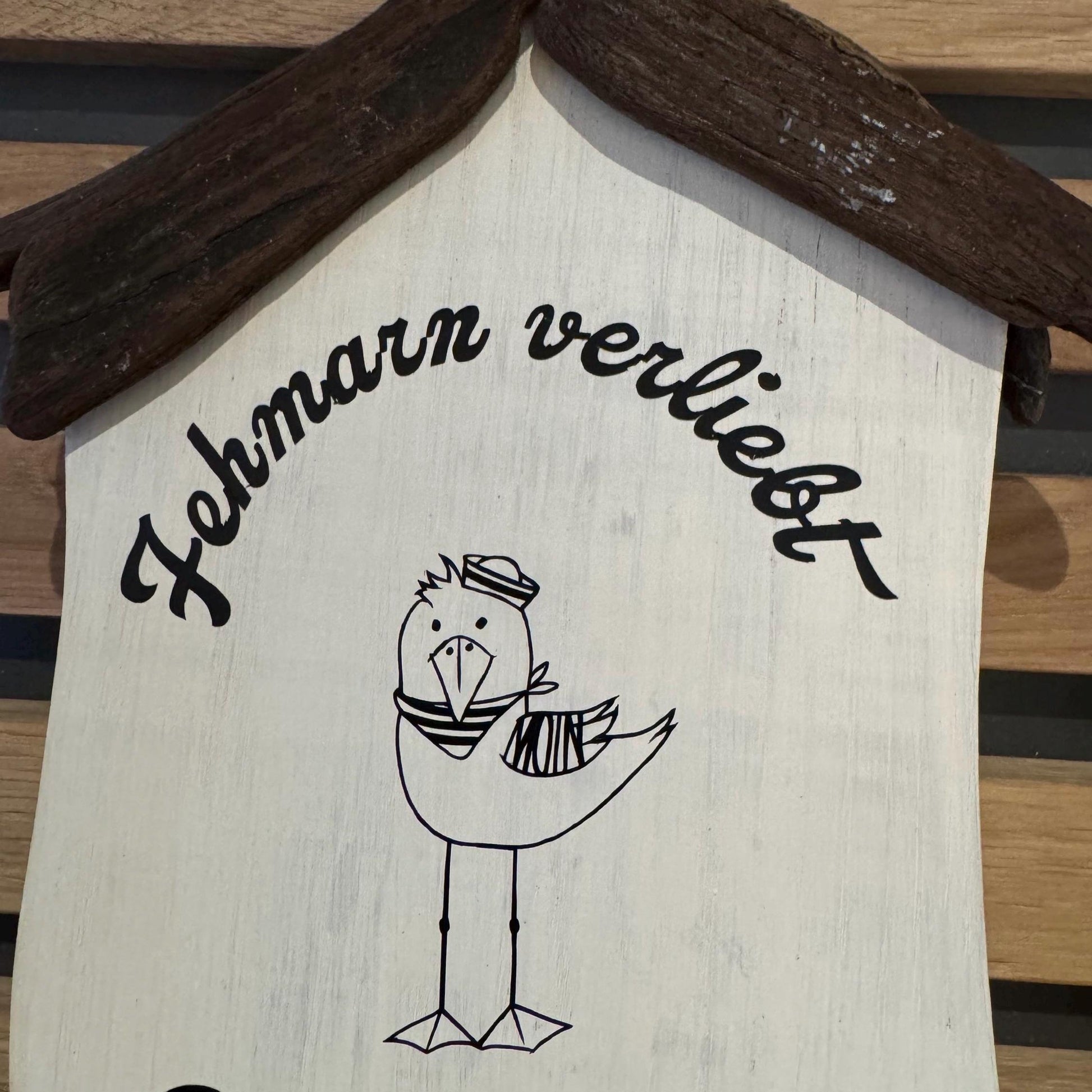 Maritimes Holzhäuschen mit Möwe, Fehmarnsundbrücke und Steinrand - gehalten in einer Hand vor heller Deko.