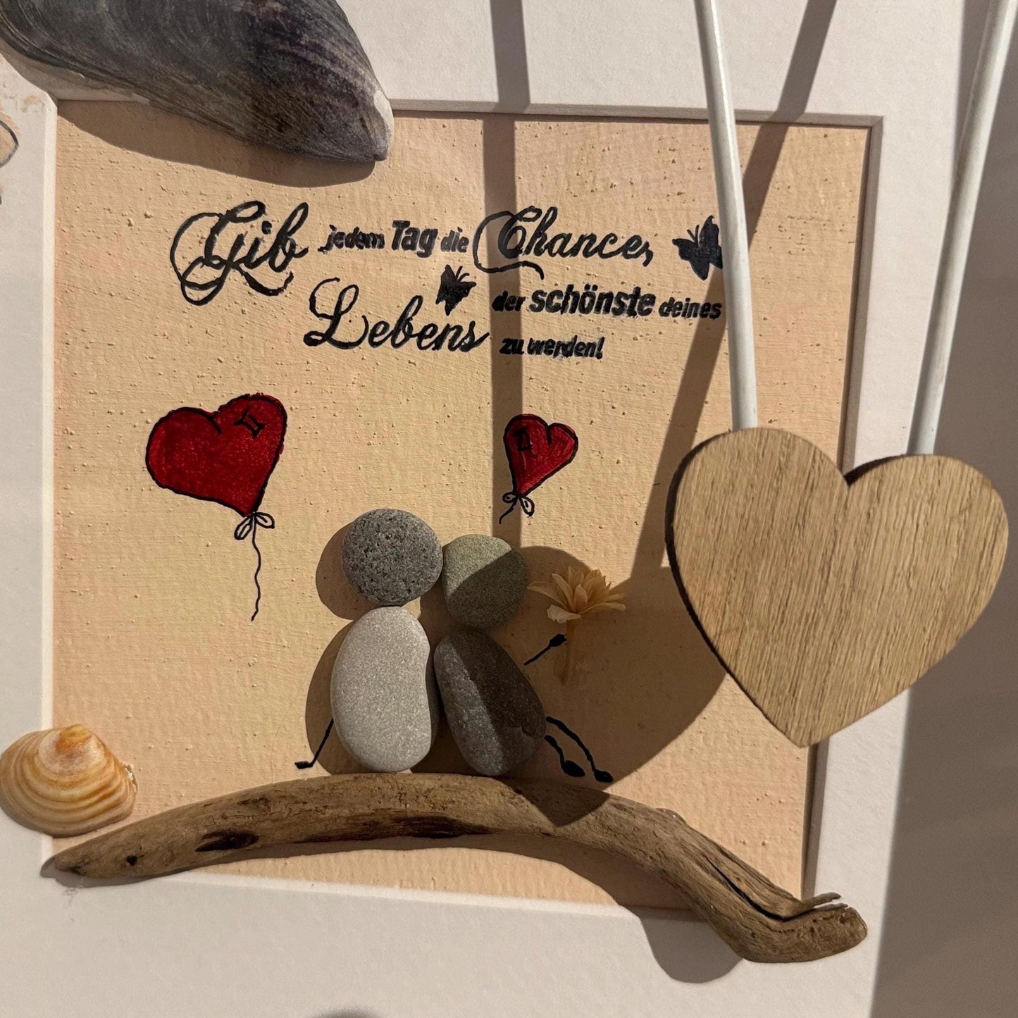 Nahaufnahme von Steinfiguren auf Treibholz mit Herzballons und Holzherz in handgefertigtem Bilderrahmen