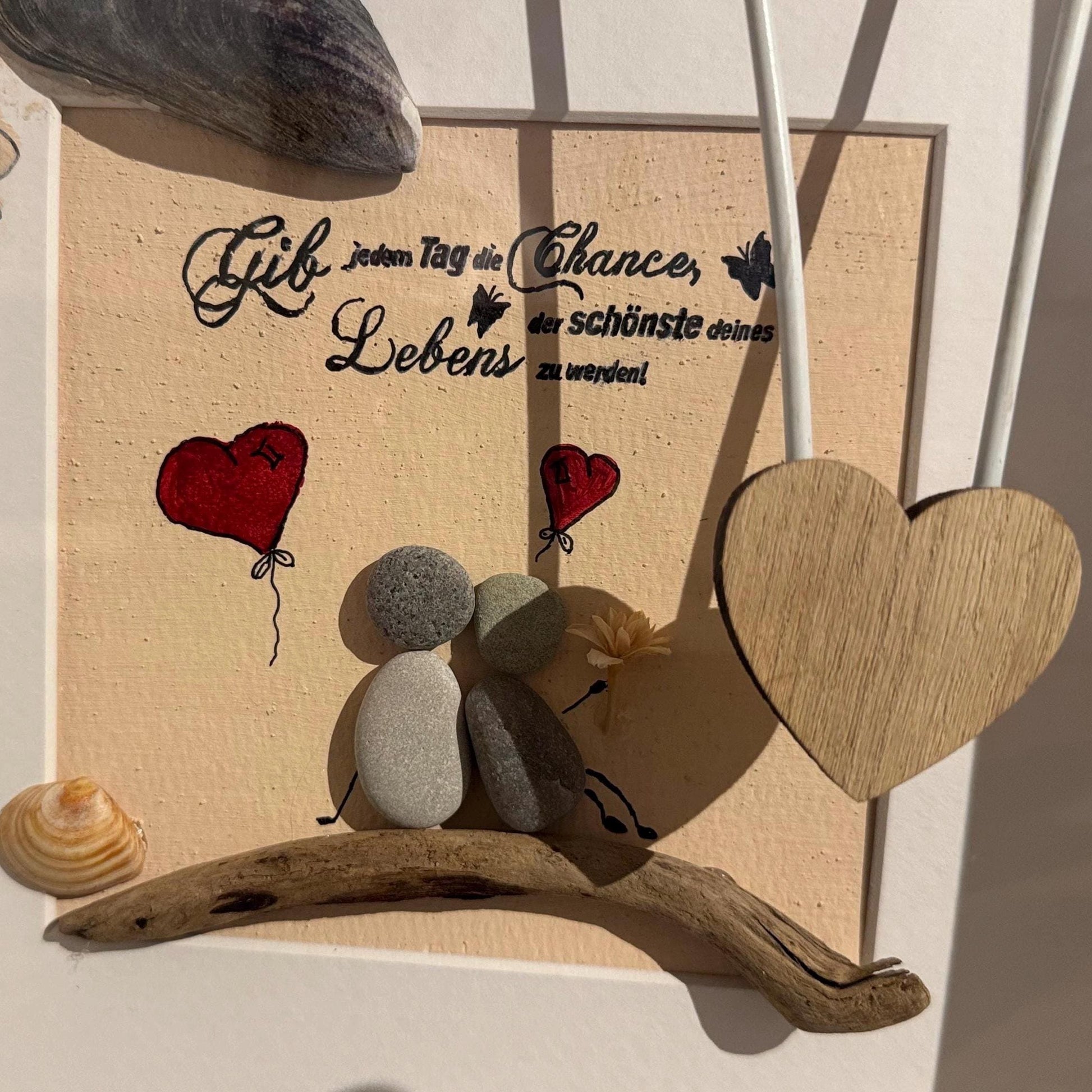 Nahaufnahme von Steinfiguren auf Treibholz mit Herzballons und Holzherz in handgefertigtem Bilderrahmen