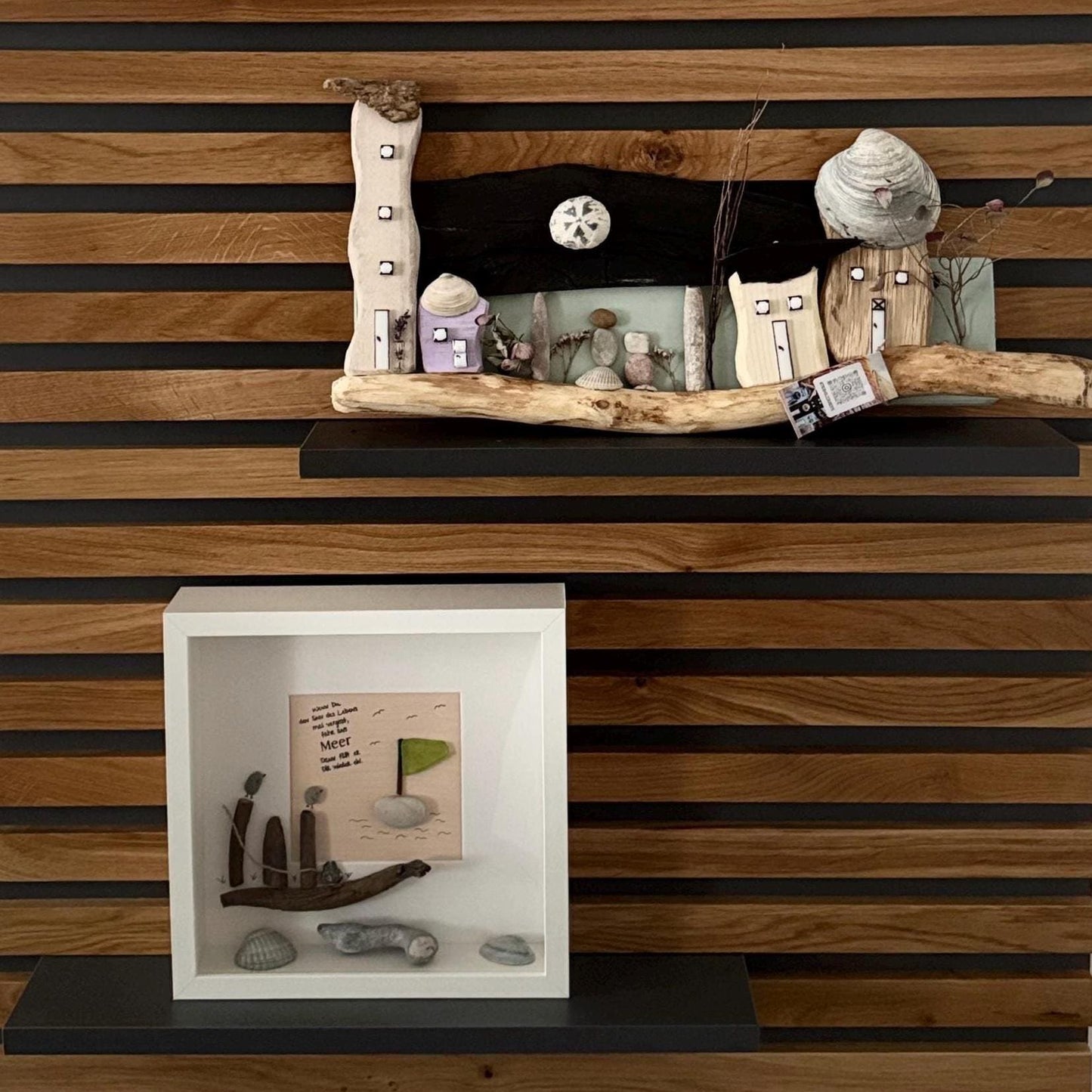 Ein Treibholz-Kunstwerk mit Miniaturhäusern und Figuren, einer Muschel und einem kleinen gerahmten Kunstwerk darunter.