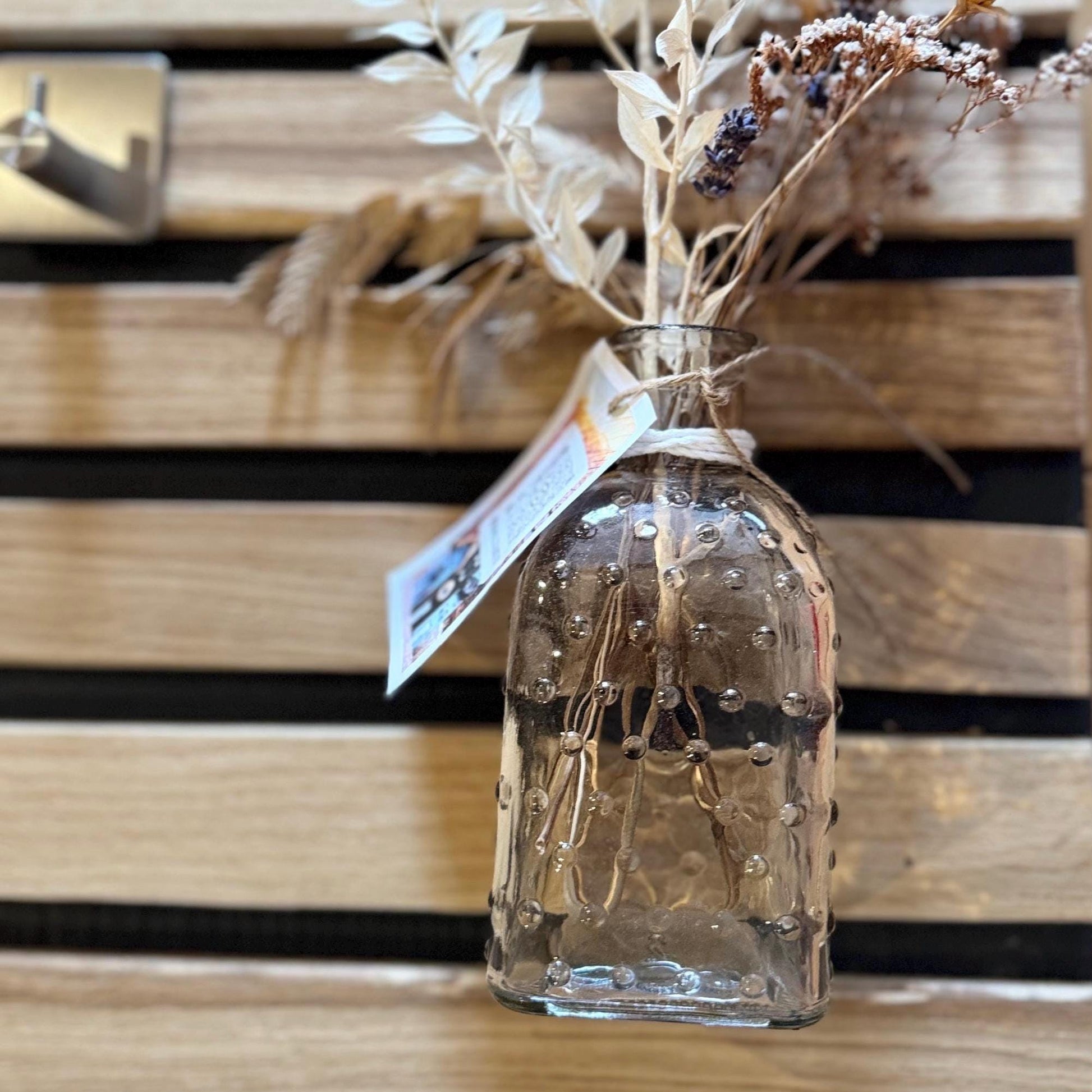 Eine klare Glasvase mit einem strukturierten, blasenartigen Muster, gefüllt mit getrockneten Blumen und Stängeln.