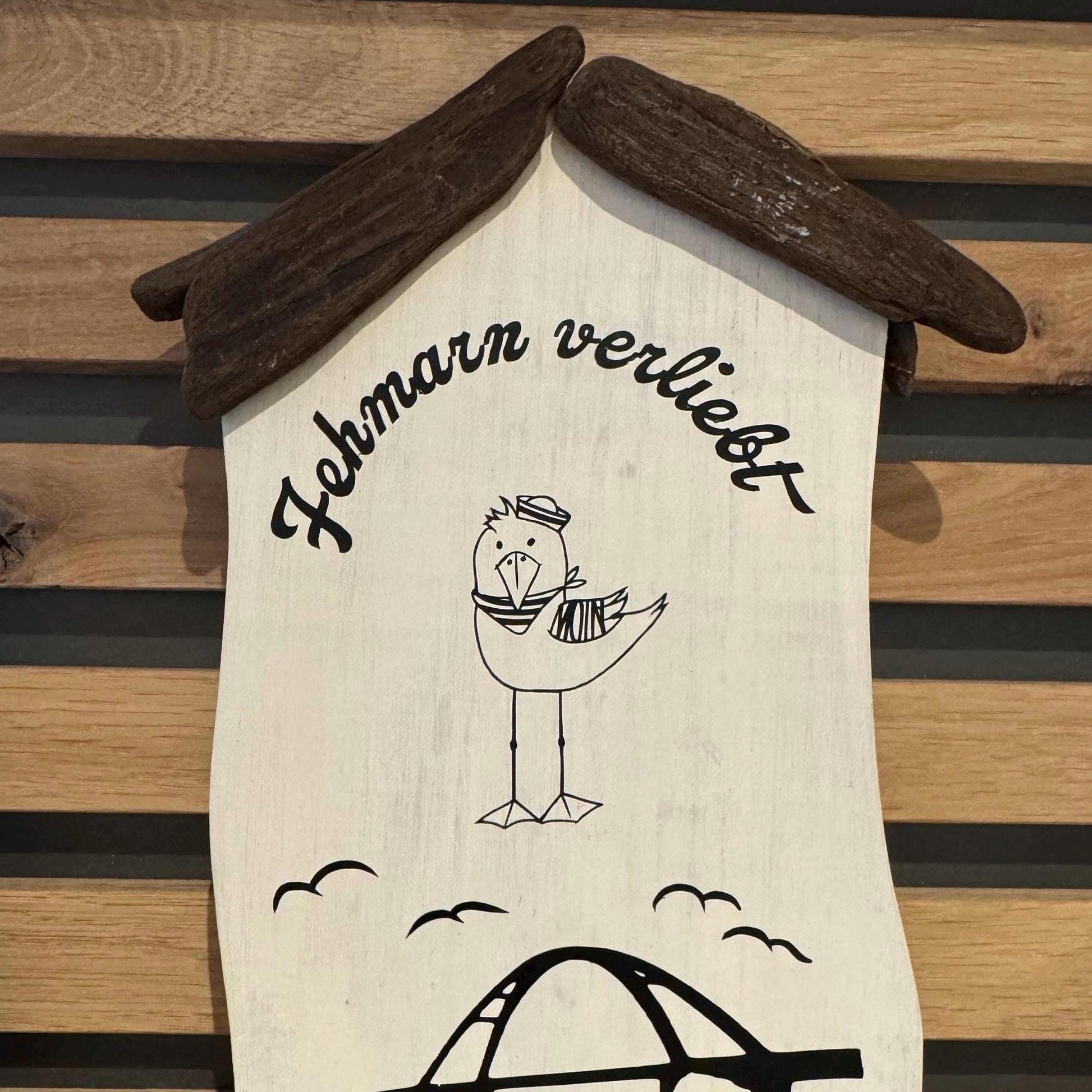 Maritimes Holzhäuschen mit Möwe, Fehmarnsundbrücke und Steinrand - gehalten in einer Hand vor heller Deko.