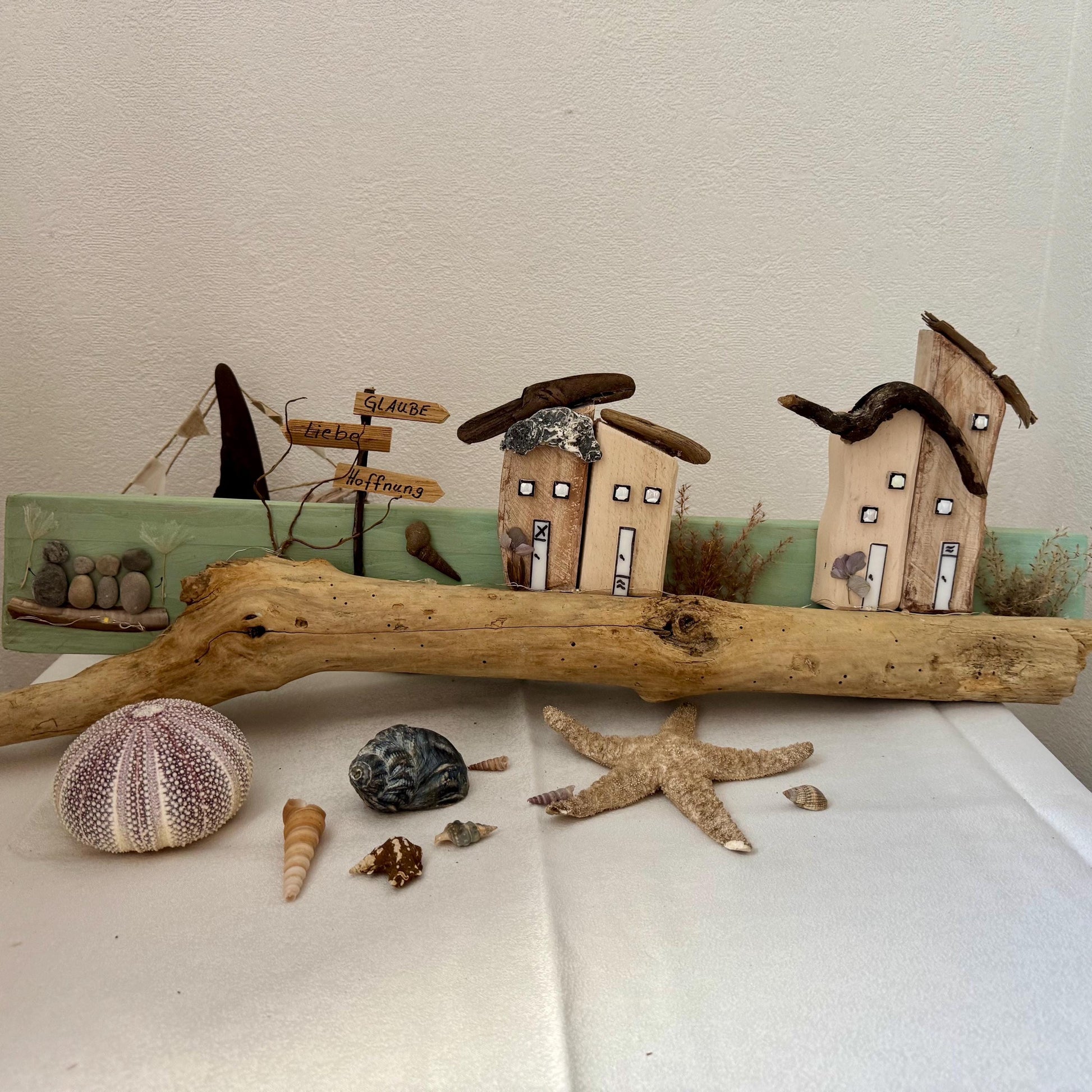 Lighted driftwood Christmas wall decoration with warm LED lights and rustic Scandinavian wooden house.