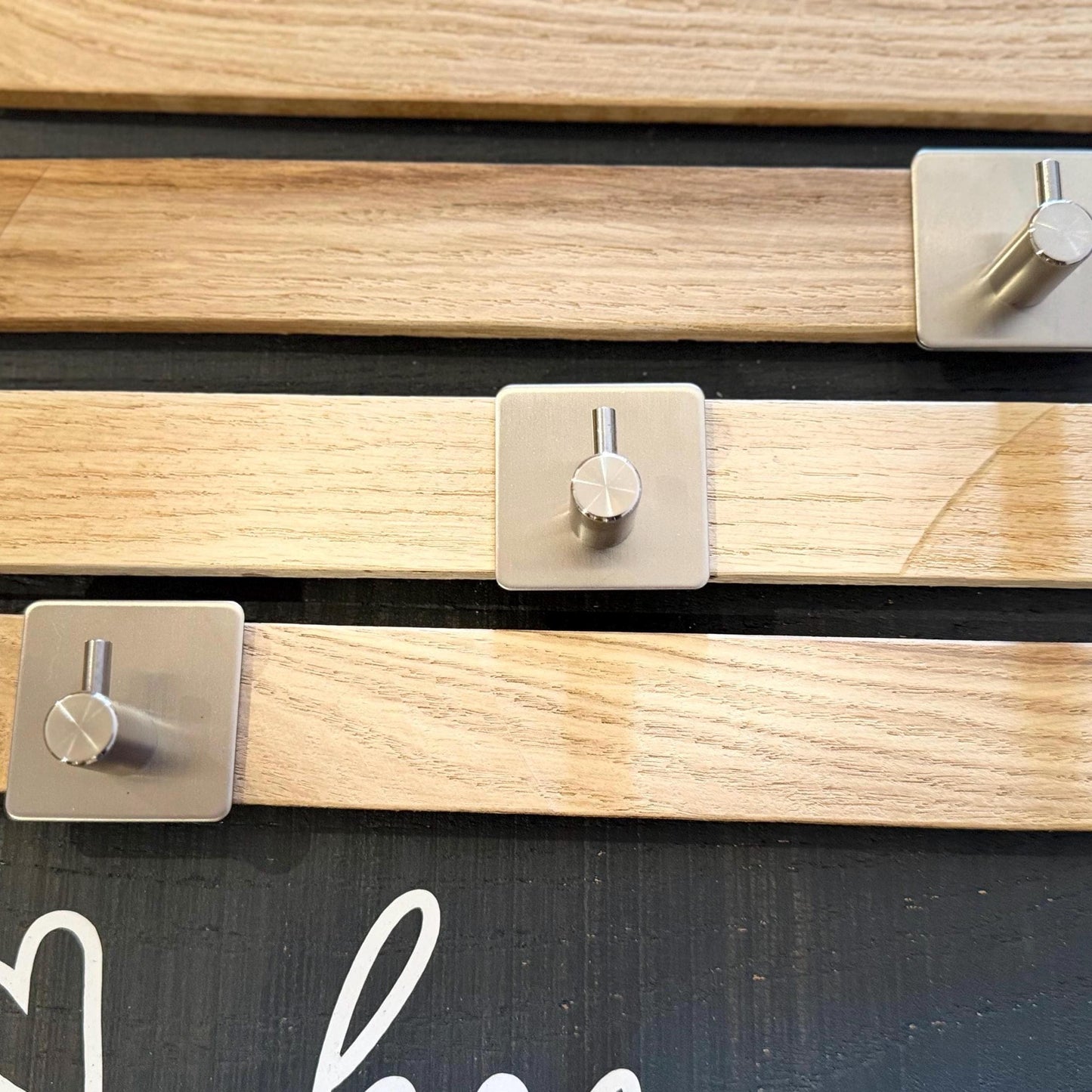 Nahaufnahme einer Wandpaneele aus Holz mit drei silbernen Metallhaken sowie horizontale Holzlatten mit natürlicher Maserung.