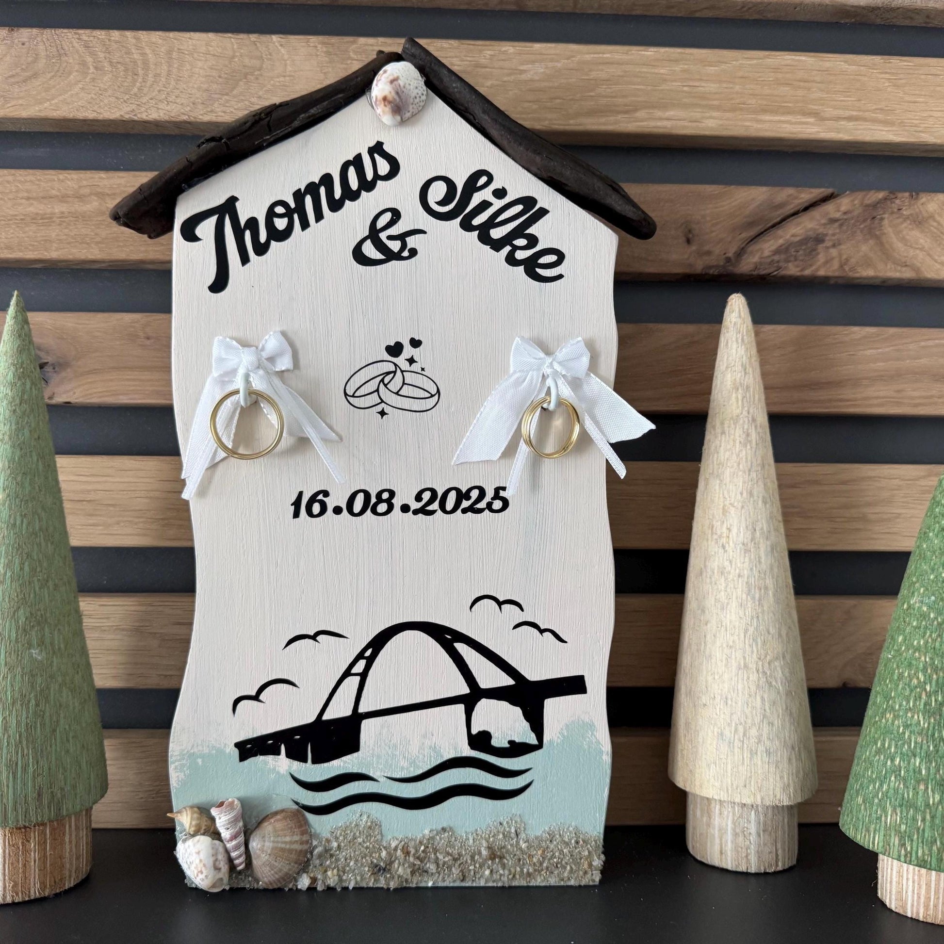 Ein personalisierter Hochzeitsringhalter aus Holz in Form eines Hauses mit den Namen "Thomas & Silke" in schwarzer Schrift.
