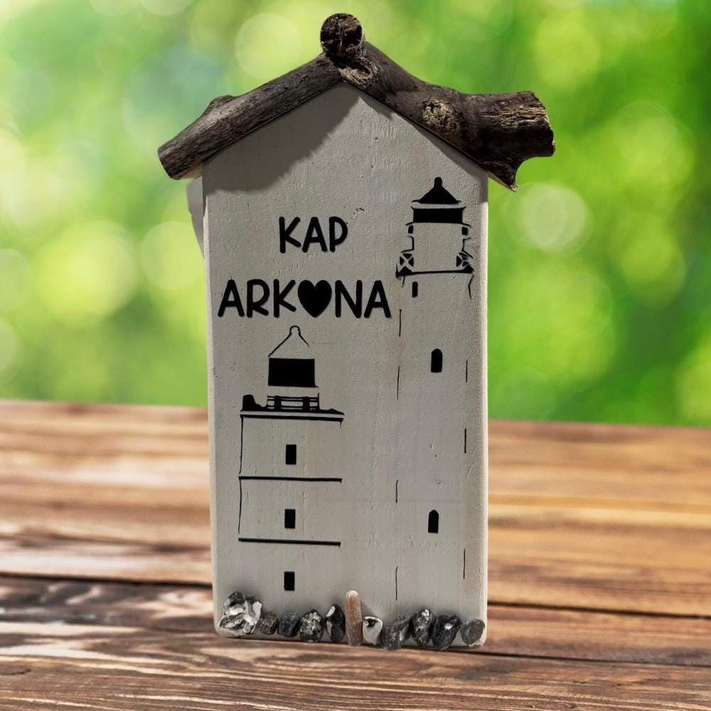 Eine weiße, holzgeschnitzte Leuchtturm-Dekoration mit dem Text "KAP ARKONA" und Leuchtturm-Illustrationen