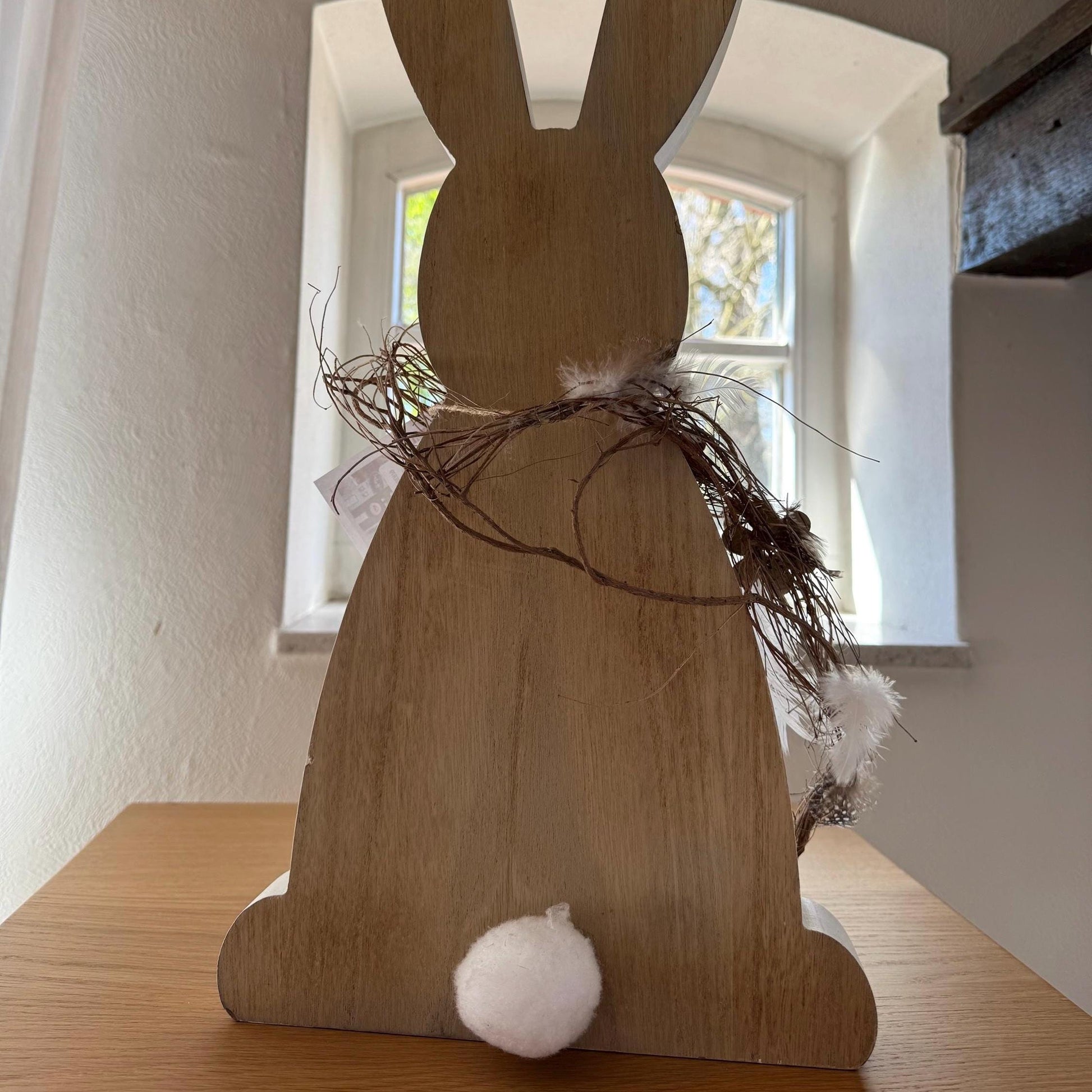 Schräg fotografierte Rückansicht des handgefertigten Osterhasen aus Holz in hellem Raum