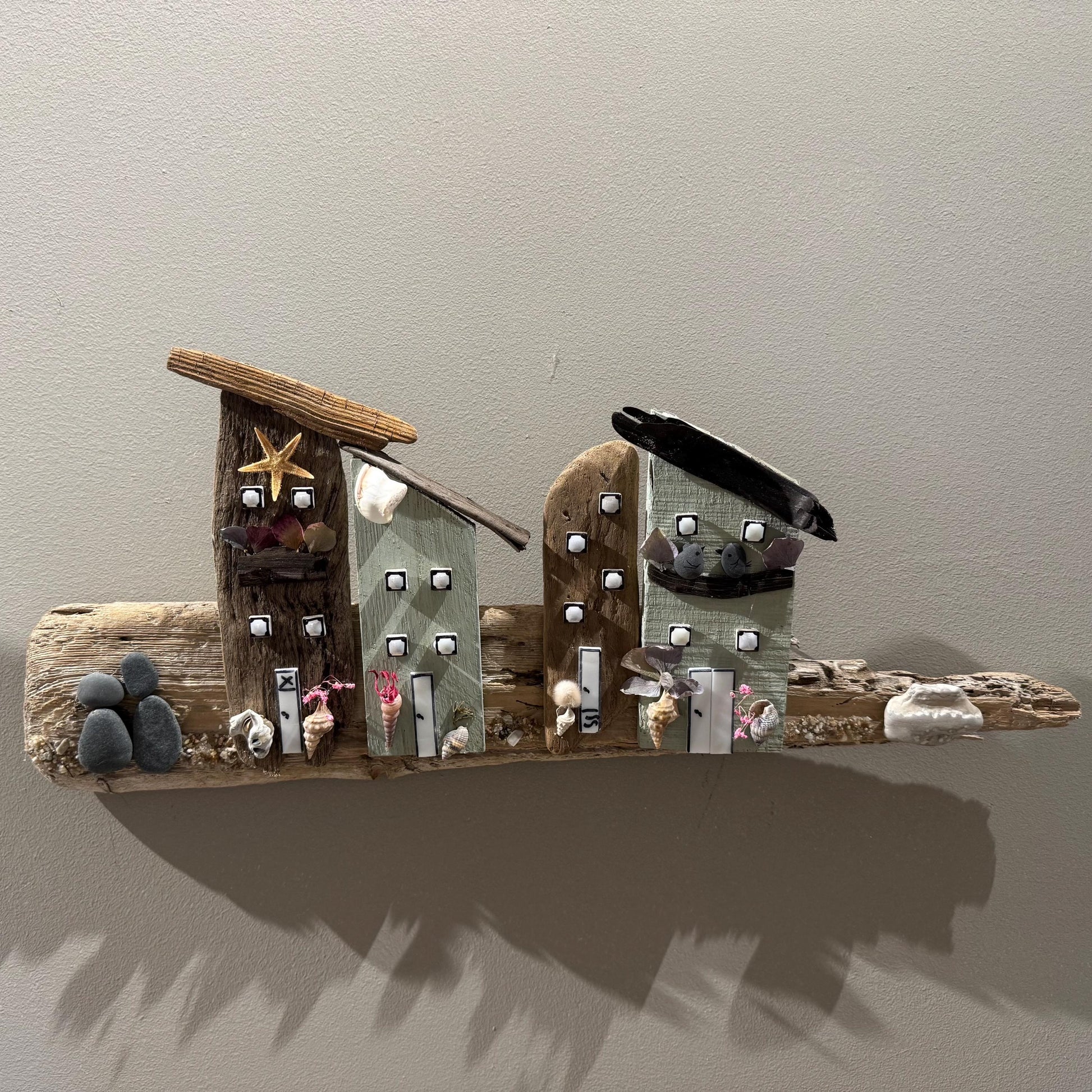 Ein Kunstwerk aus Treibholz mit Miniaturhäusern mit Holz- und Muscheldetails. Das Werk ist auf einem Stück Treibholz montiert
