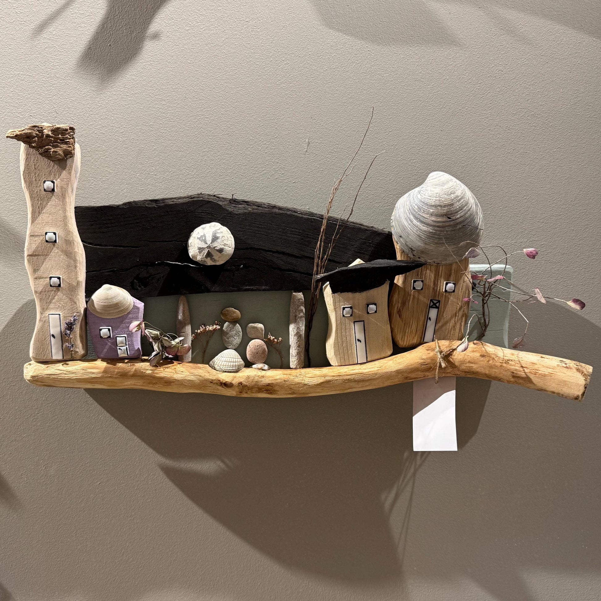 Ein Kunstwerk aus Treibholz mit Miniatur-Holzhäusern, Muscheln und einem Seestern.