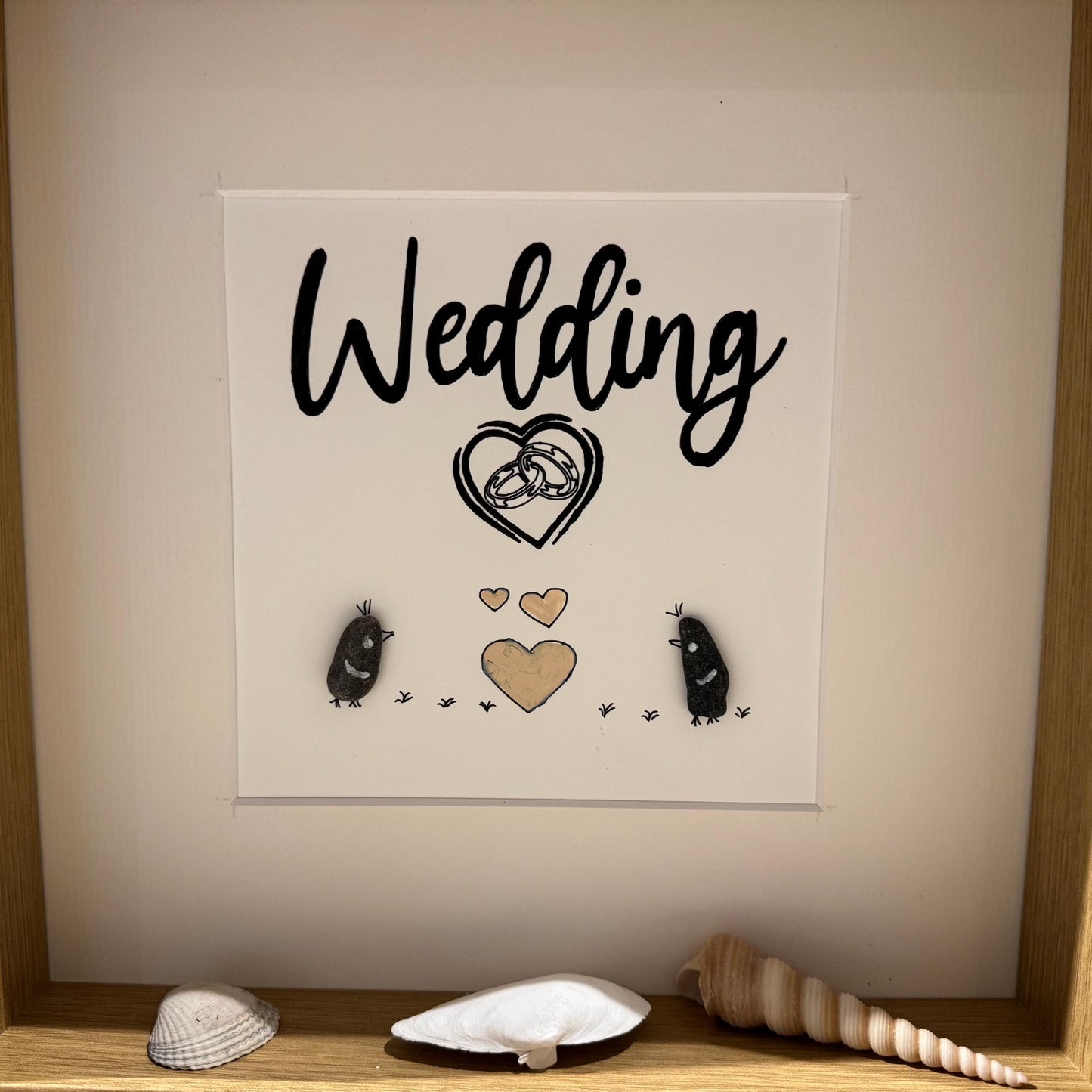 Ein gerahmtes Kunstwerk zum Thema Hochzeit. Das Kunstwerk zeigt das Wort "Wedding" in schwarzer Schrift über einem Herzen