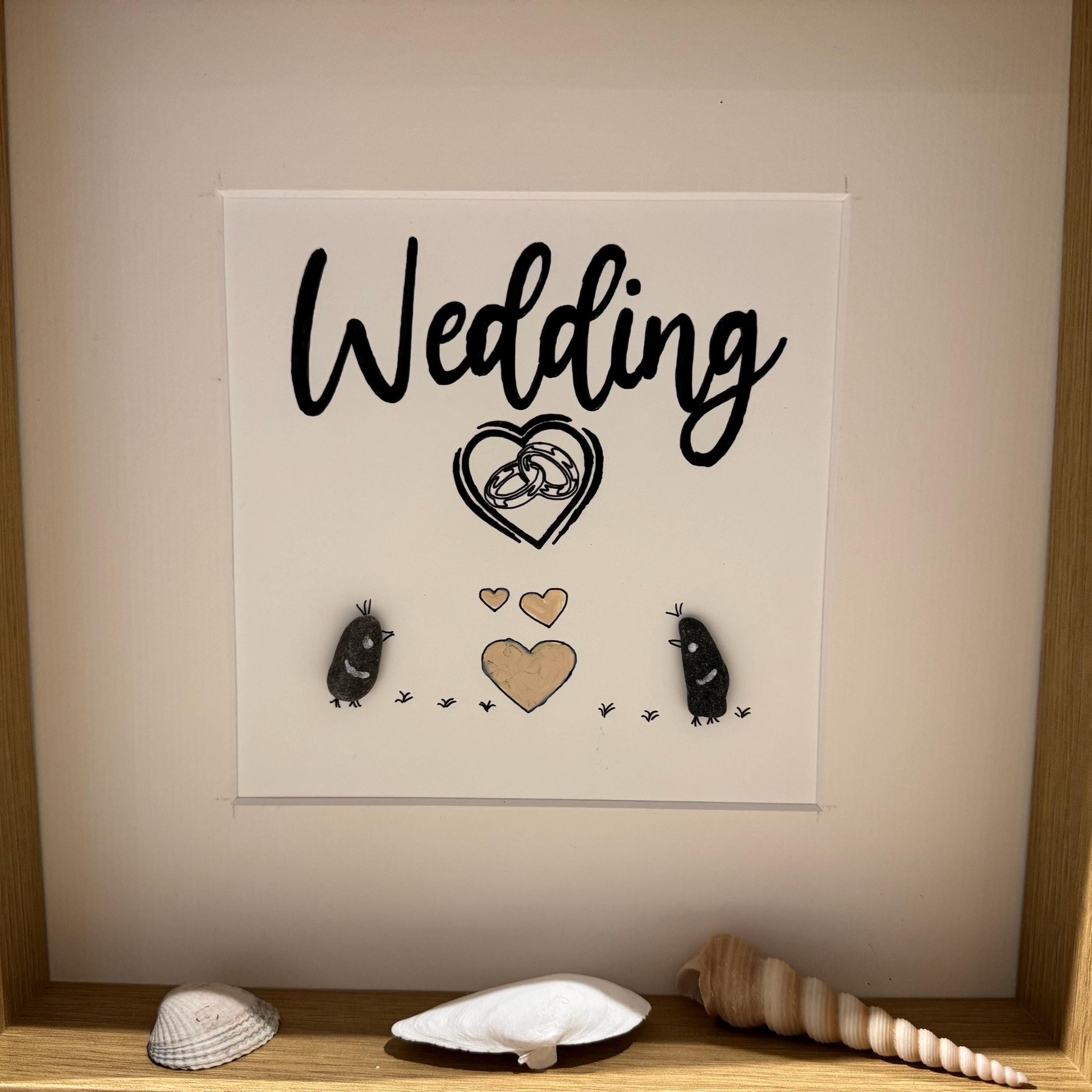 Ein gerahmtes Kunstwerk zum Thema Hochzeit. Das Kunstwerk zeigt das Wort "Wedding" in schwarzer Schrift über einem Herzen