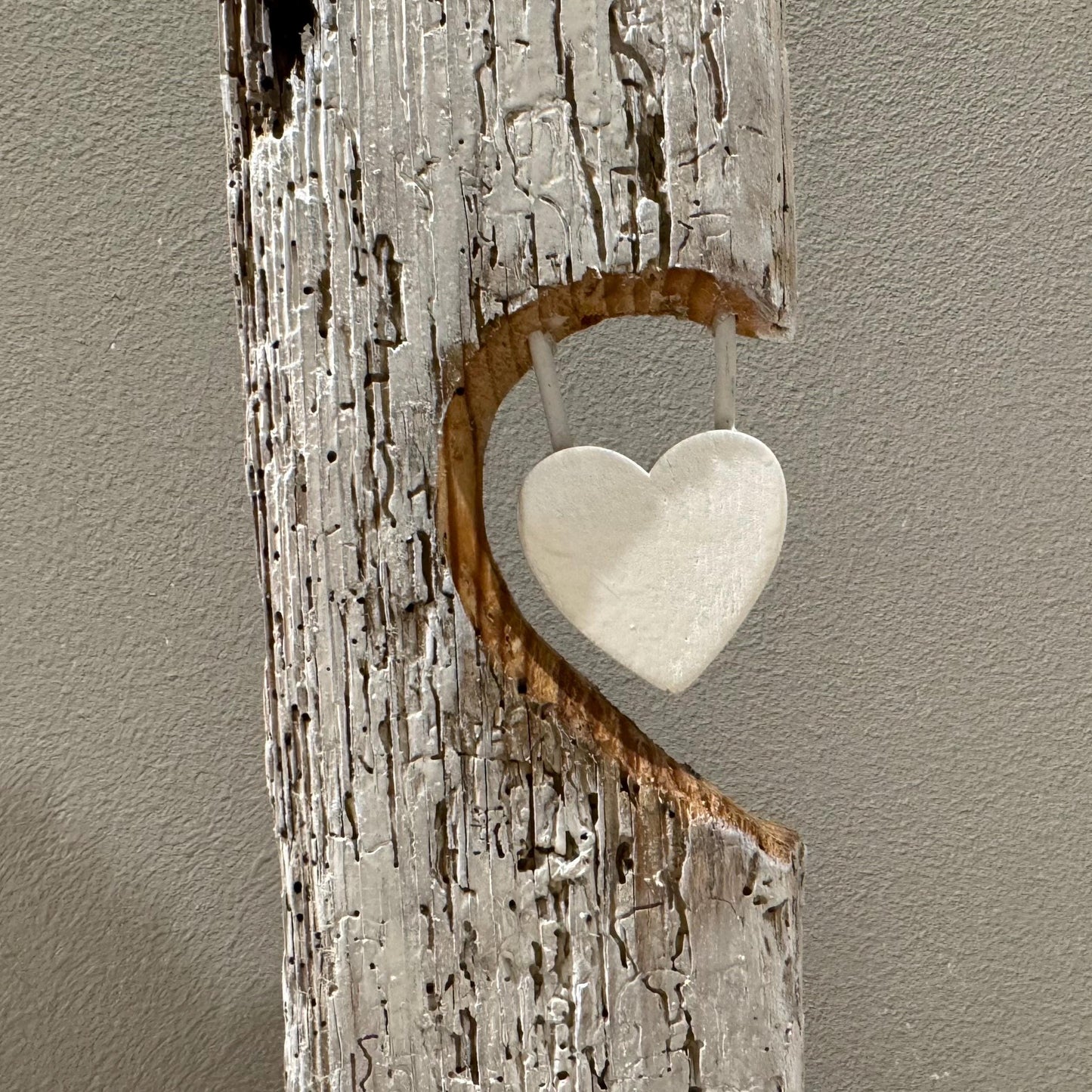 Eine rustikale Holzskulptur mit herzförmigem Ausschnitt und einem hängenden weißen Herzen.