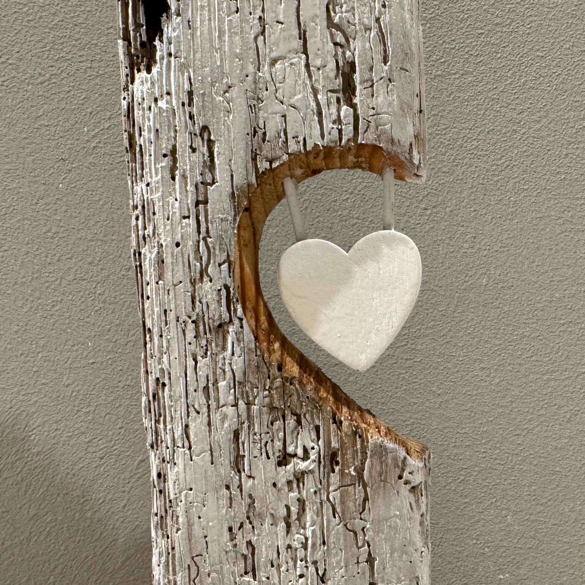 Eine rustikale Holzskulptur mit herzförmigem Ausschnitt und einem hängenden weißen Herzen.