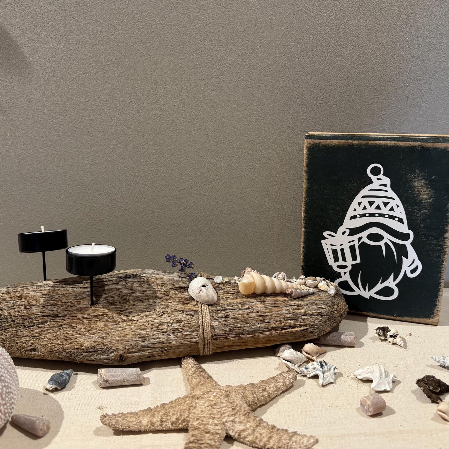 Rustikale Weihnachtsdeko aus Holz mit weißem Wichtel-Motiv auf schwarzem Holzblock, dekoriert im hellen skandinavischen Raum.