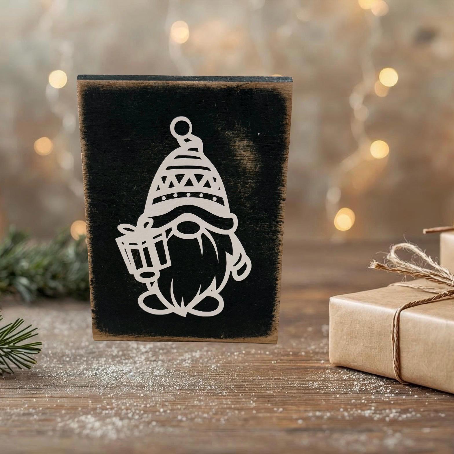 Rustikales Holzschild mit weißem Weihnachtswichtel-Motiv, dekoriert vor einem warmen, Hintergrund und natürlicher Winterdeko.