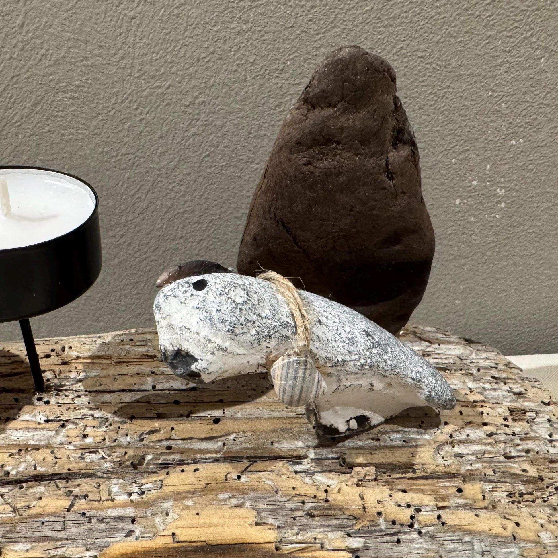 Eine skurrile Steinskulptur, verziert mit Muscheln. Der graue Steinkörper hat bemalte Augen und eine kleine Muschel oben.