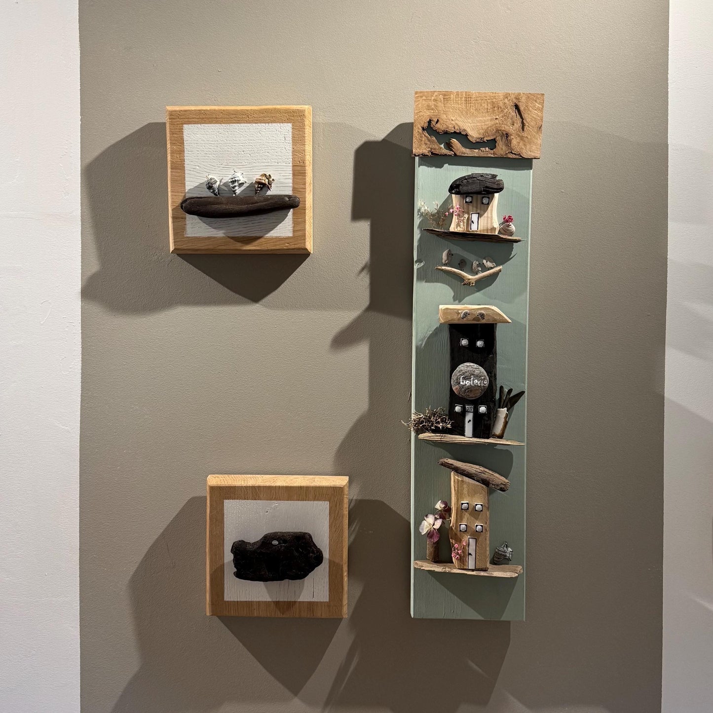 Drei Wandkunstwerke aus Holz. Ein quadratisches Stück zeigt eine dunkle, organische Form  von Treibholzzauber79