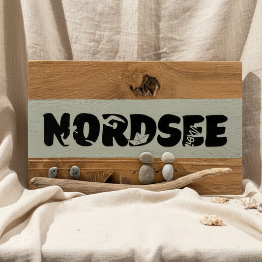 Holzschild mit dem Wort "NORDSEE" in Schwarz. Das Schild hat einen hellgrünen Streifen und zeigt Kieselkunstfiguren.