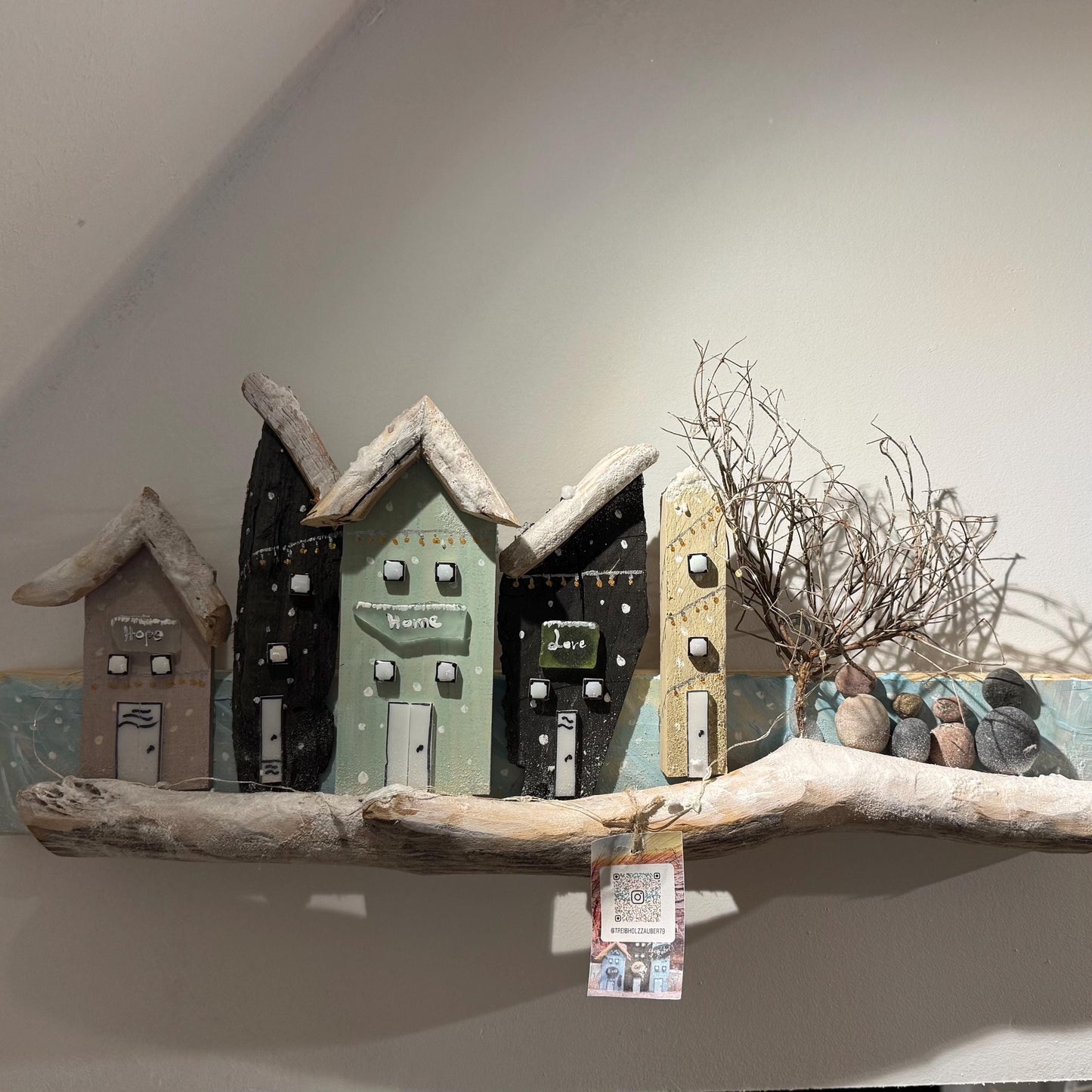 Ein Holz-Kunstwerk mit Küsten-Thema, das Miniaturhäuser in verschiedenen Farben zeigt mit Treibholz-Dächern