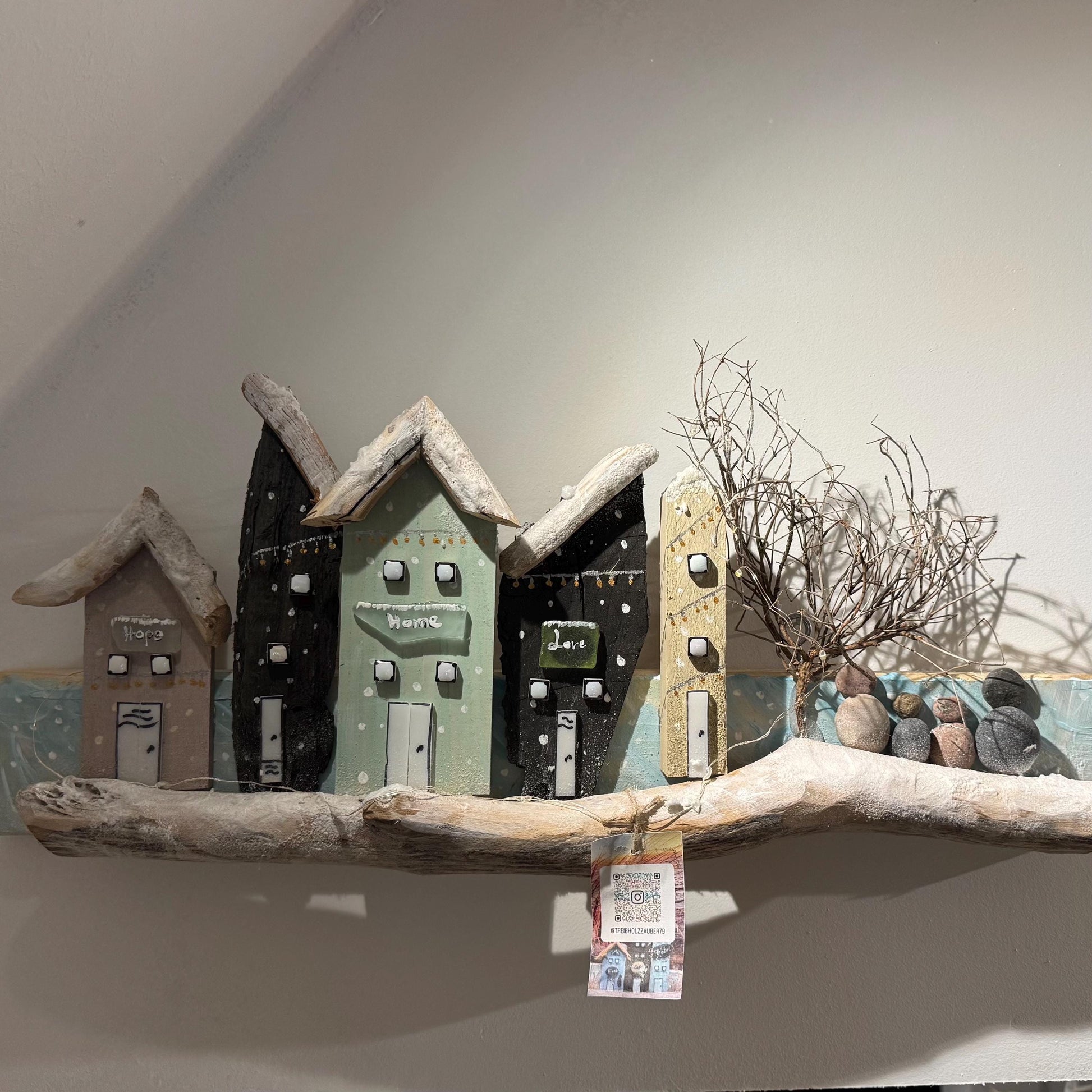 Ein Holz-Kunstwerk mit Küsten-Thema, das Miniaturhäuser in verschiedenen Farben zeigt mit Treibholz-Dächern