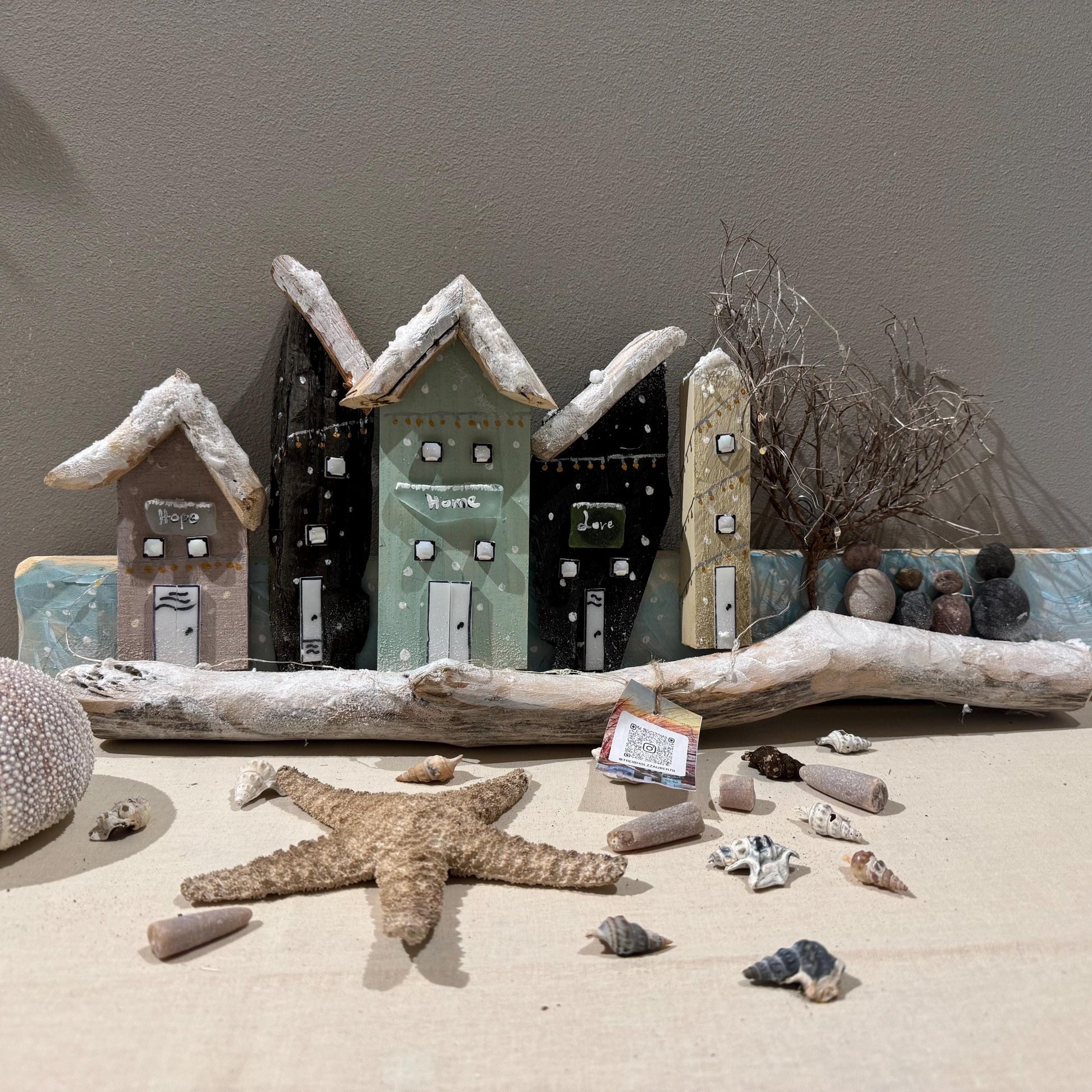 Handgemachtes Wandbild aus Treibholz mit kleinen bunten Holzhäusern im Winterdesign, dekoriert mit Schneeeffekt