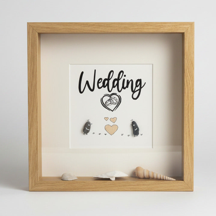 Ein gerahmtes Kunstwerk mit dem Wort "Wedding" in schwarzer Schrift. Das Kunstwerk zeigt ein Herz mit Eheringen