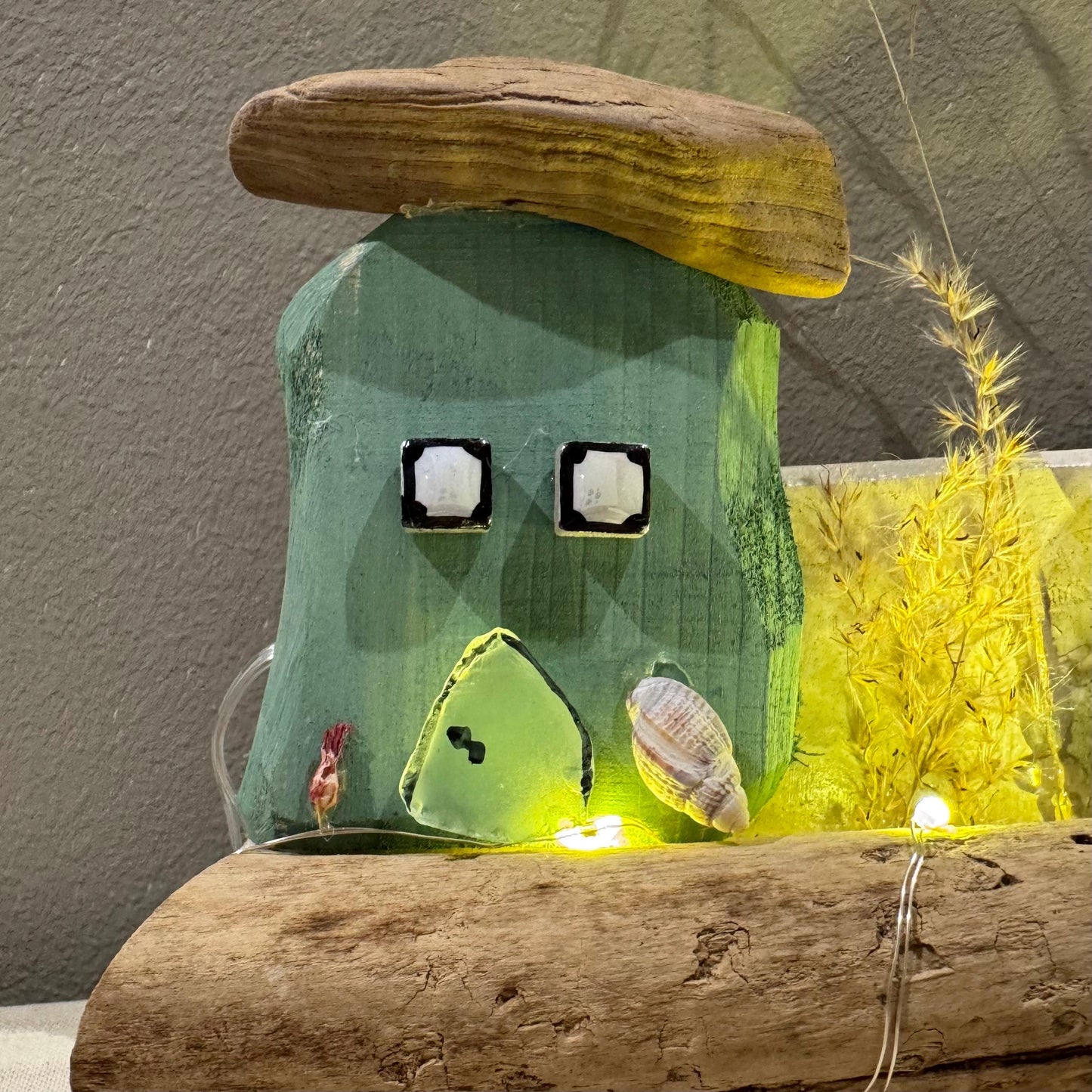 Treibholz Wanddeko Haus aus Treibholz mit kleinen Minihäusern und warmen LED-Lichtern auf heller Wand, maritime Dekoration.