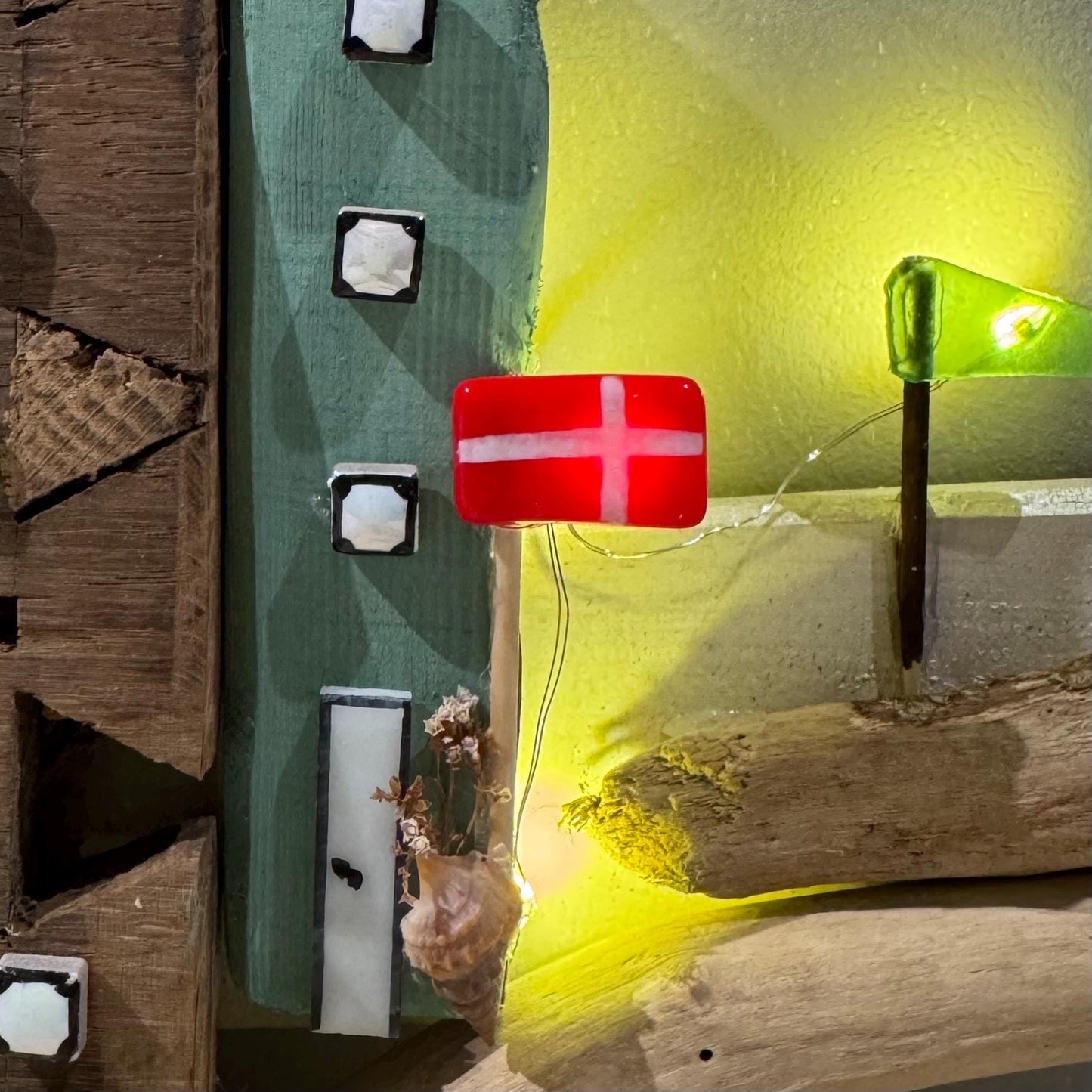 Treibholz Wanddeko Haus aus Treibholz mit kleinen Minihäusern und warmen LED-Lichtern auf heller Wand, maritime Dekoration.