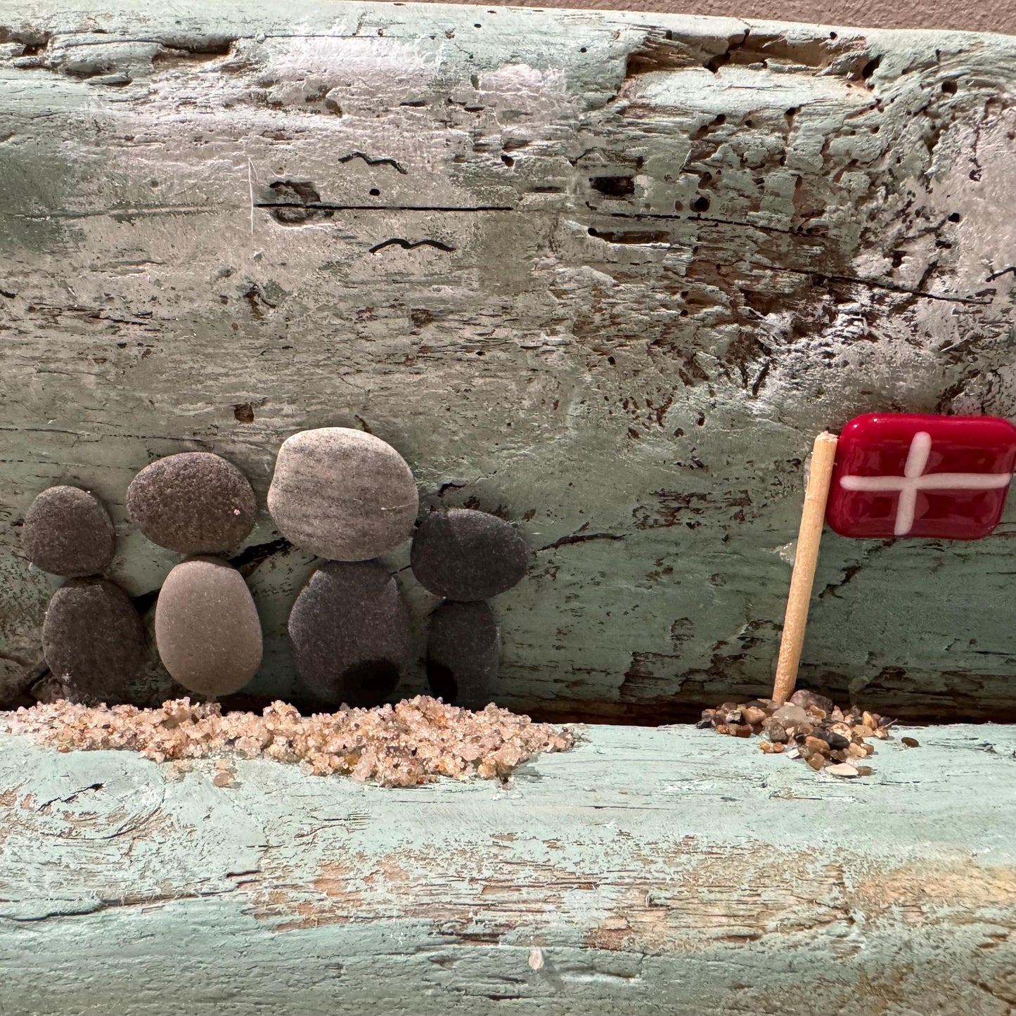 Ein Treibholz-Kunstwerk mit einer fünfköpfigen Familie aus glatten, grauen Steinen. Eine kleine dänische Flagge daneben.