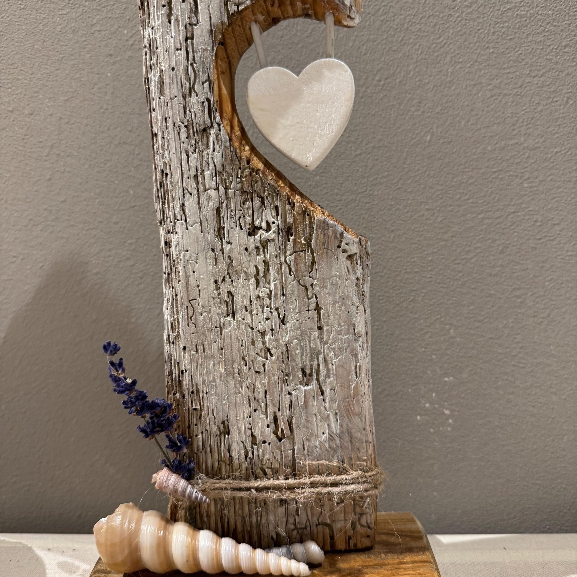 Eine rustikale Holzskulptur mit herzförmigem Ausschnitt und einem hängenden weißen Herzen sowie einer Muschel verziert.