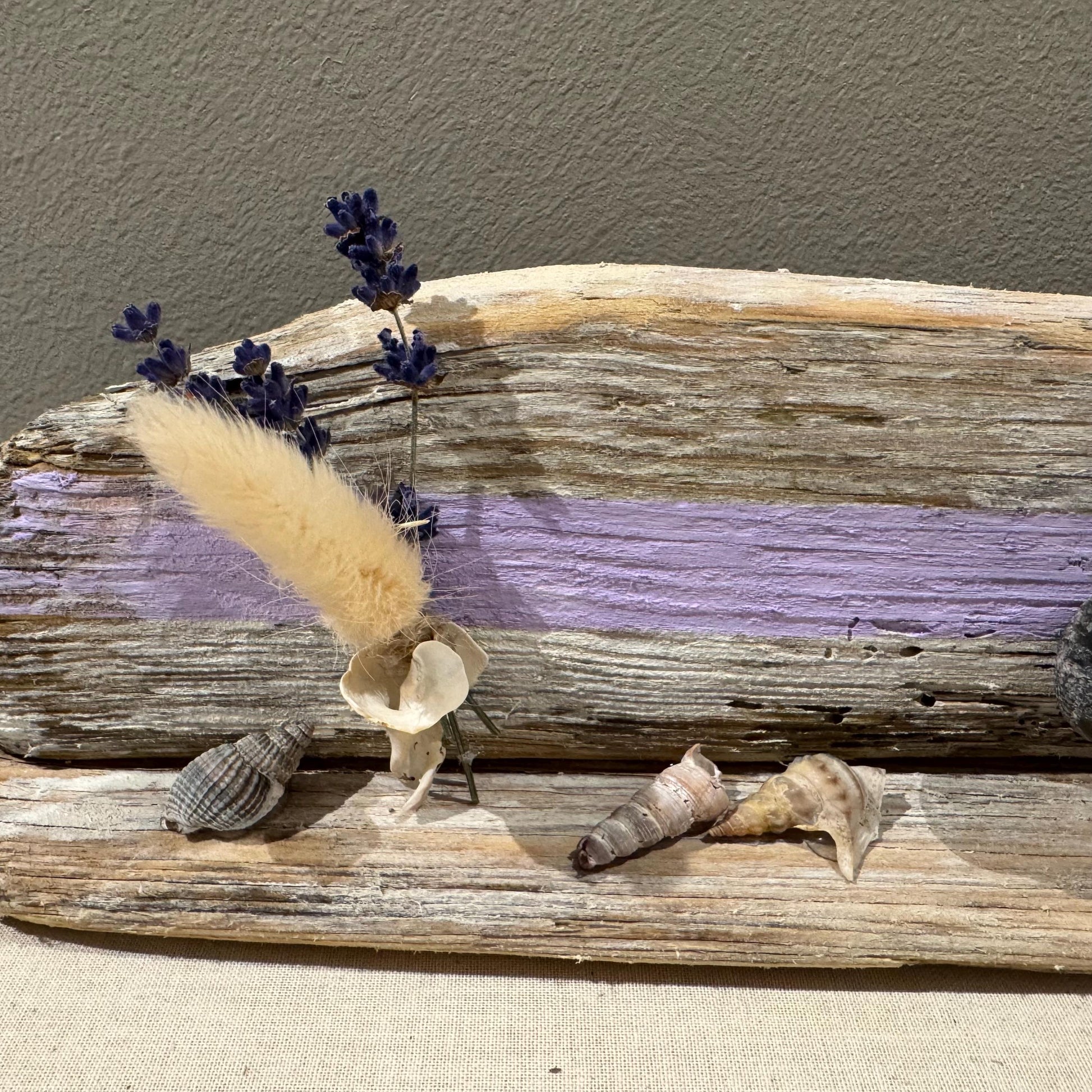 Maritime Treibholz Deko mit kleiner Steinfigur und Muscheln, liebevoll arrangiert auf Treibholz vor einer gemütlichen Couch.