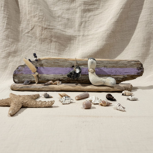 Maritime Treibholz Deko mit kleiner Steinfigur und Muscheln, liebevoll arrangiert auf Treibholz vor einer gemütlichen Couch.