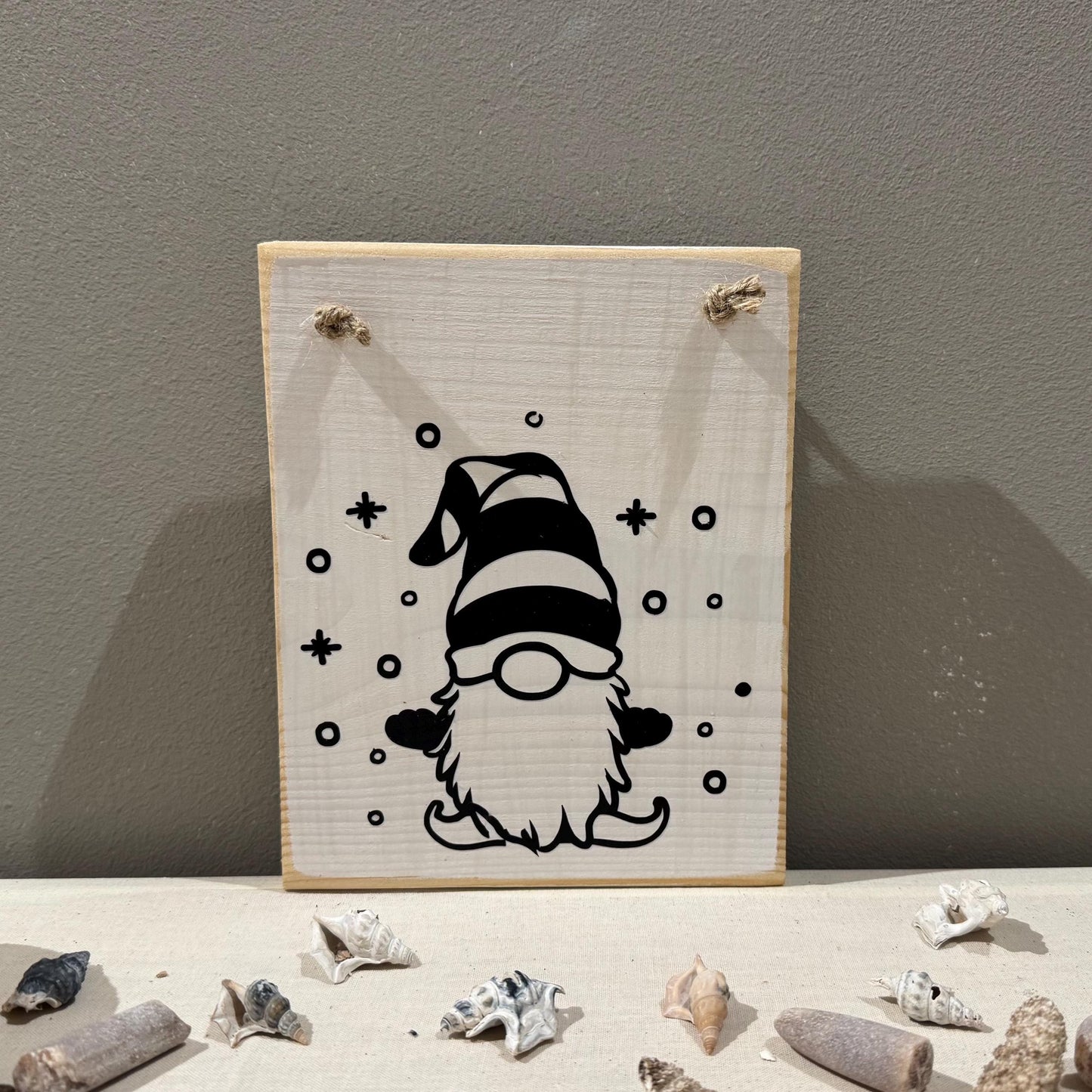 Ein Holzschild mit einer schwarz-weißen Zwergenillustration. Der Zwerg hat einen gestreiften Hut und einen langen weißen Bart