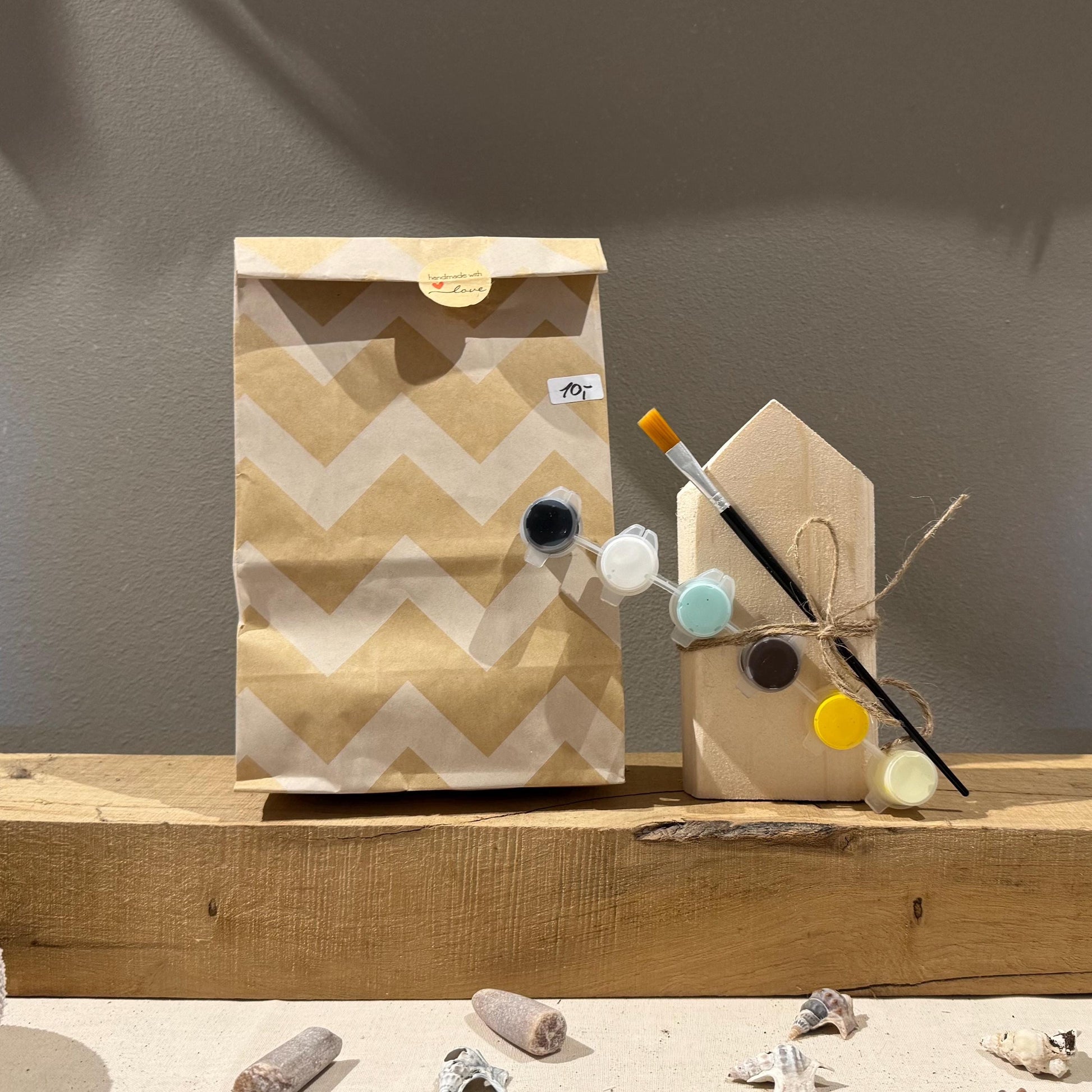 Ein Bastelset mit einem Holzhaus, Farbtöpfen und einem Pinsel. Das Haus ist mit  enthält eine Farbpalette