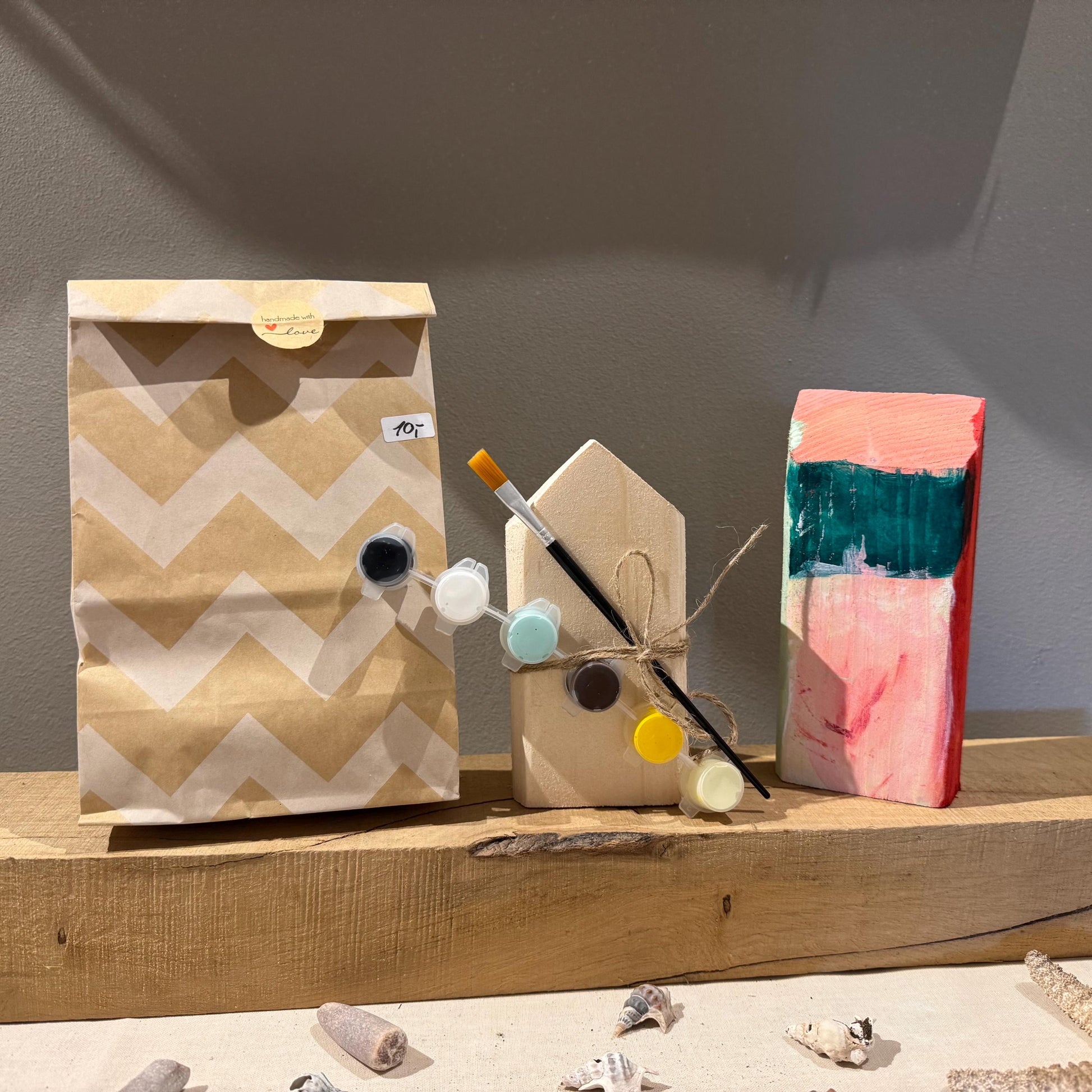 DIY Set Holzhaus bemalen enthält ein unbehandeltes Holzhaus, 6 Farben, einen Pinsel und Muscheln.