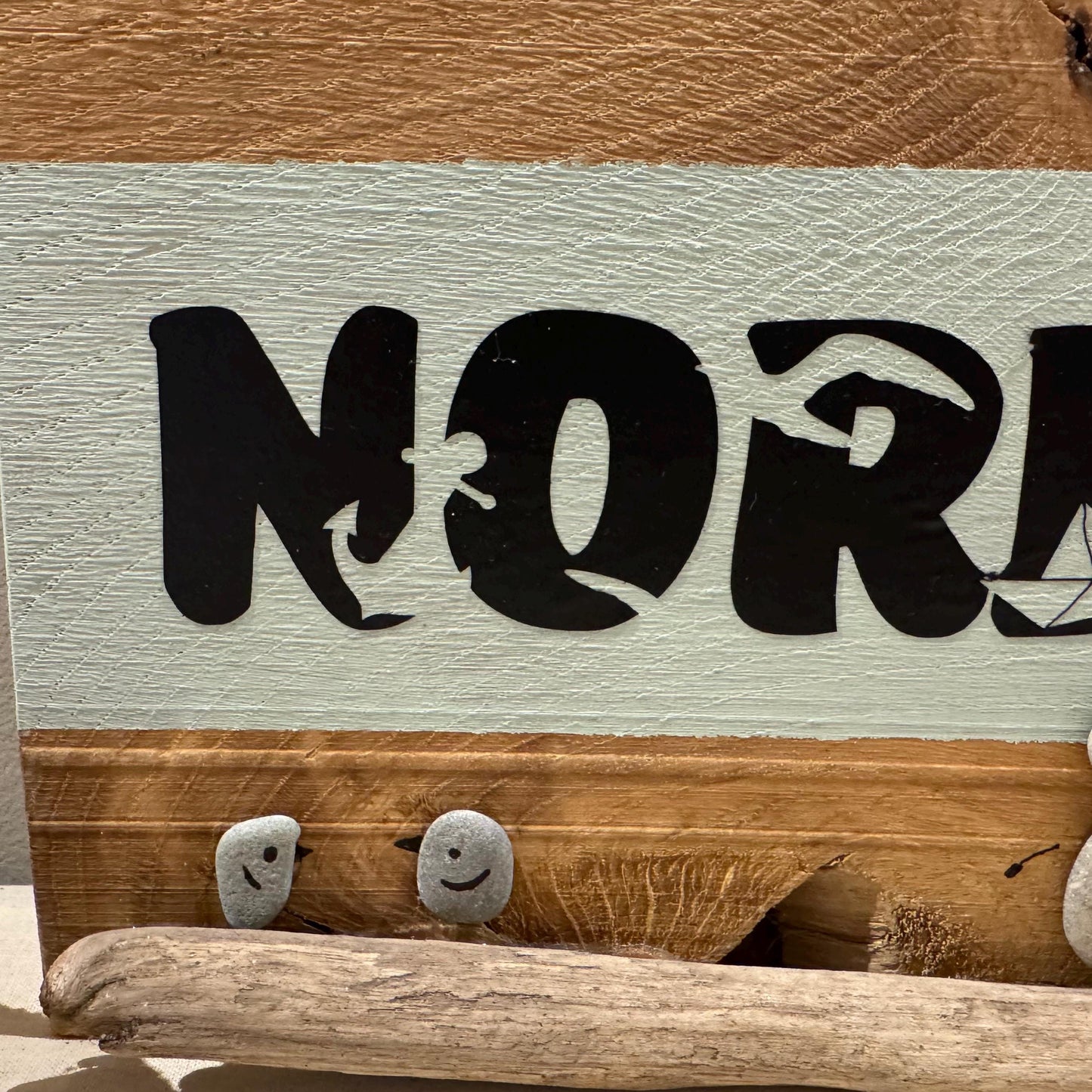 Holzschild mit dem Wort "NORDSEE" in schwarzen Buchstaben. Das Schild hat einen hellblauen Hintergrund mit einem Holzrahmen.