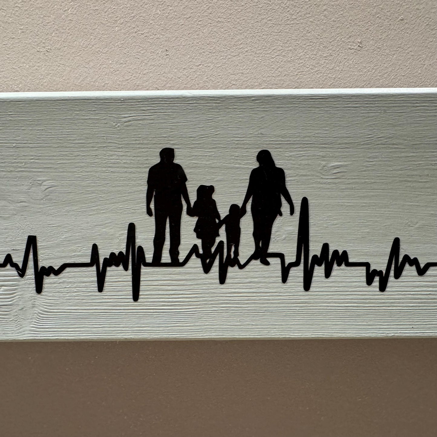 Schwarze Silhouette einer vierköpfigen Familie, die zusammen spaziert, vor einem hellgrauen Holzgrund von Treibholzzauber79