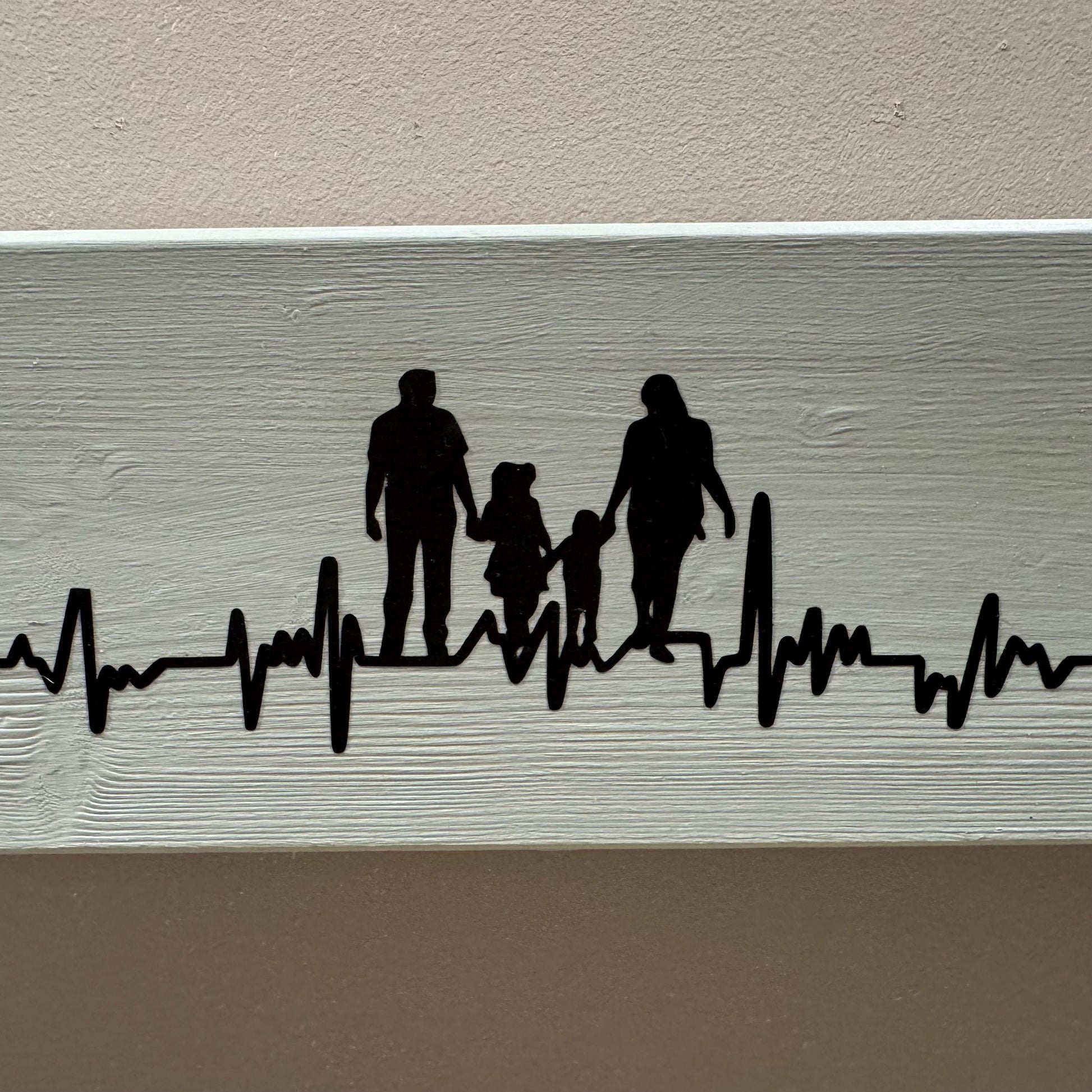 Schwarze Silhouette einer vierköpfigen Familie, die zusammen spaziert, vor einem hellgrauen Holzgrund von Treibholzzauber79
